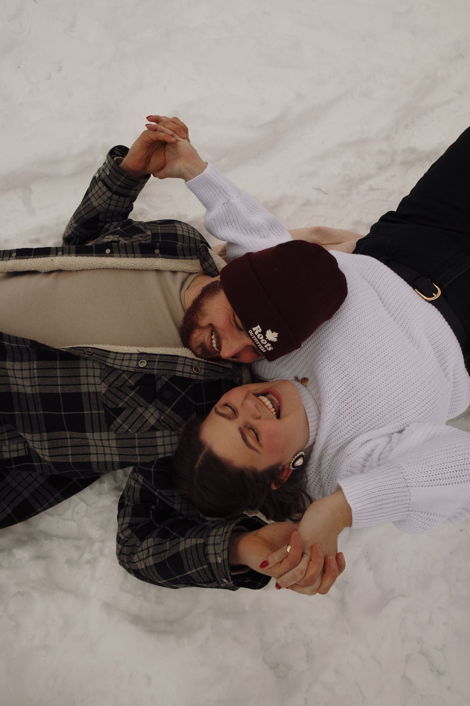 Couple lying in snow wearing winter clothing sharing laughter together.