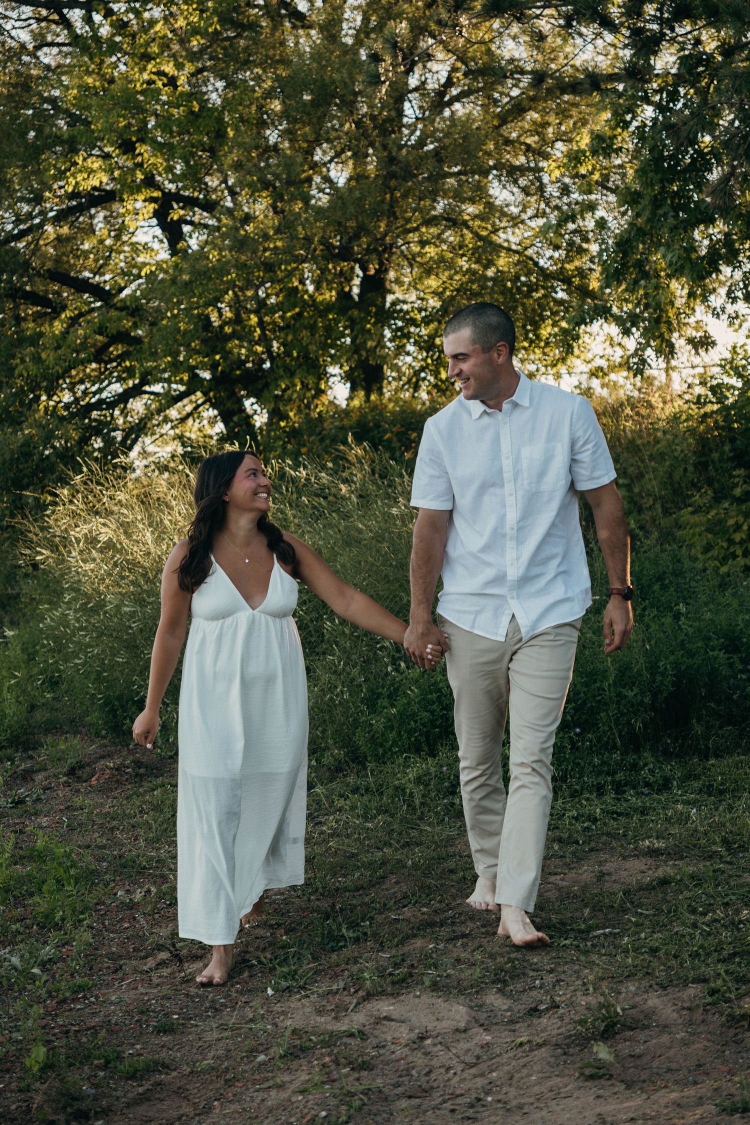 A couple walking together on a grassy hillside wearing coordinated white and beige outfits.
