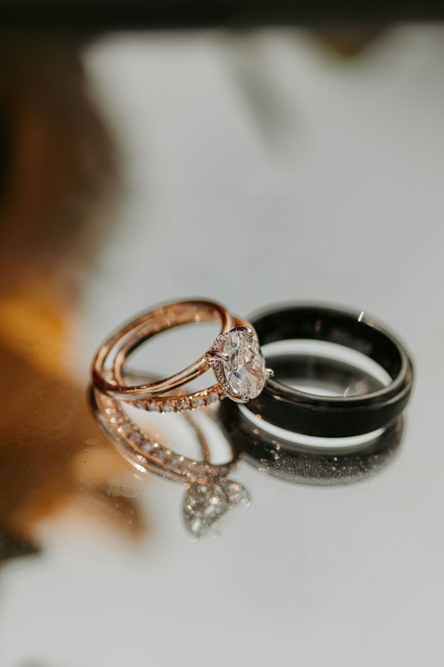 Rose gold engagement ring with diamonds sits next to a black band on white surface.