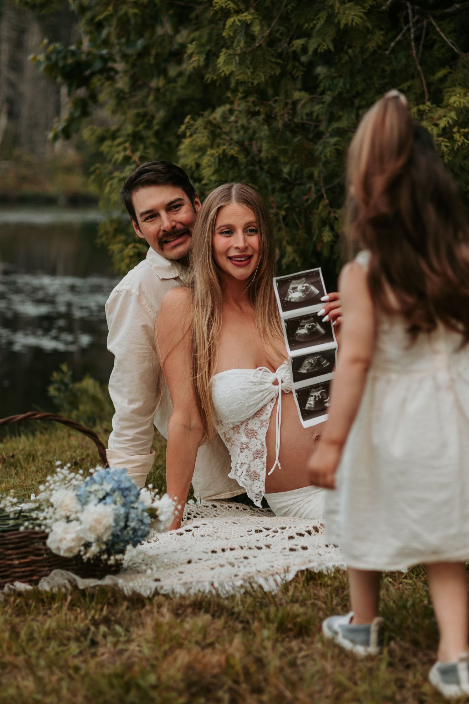 Family sharing ultrasound photos during outdoor pregnancy announcement photoshoot.