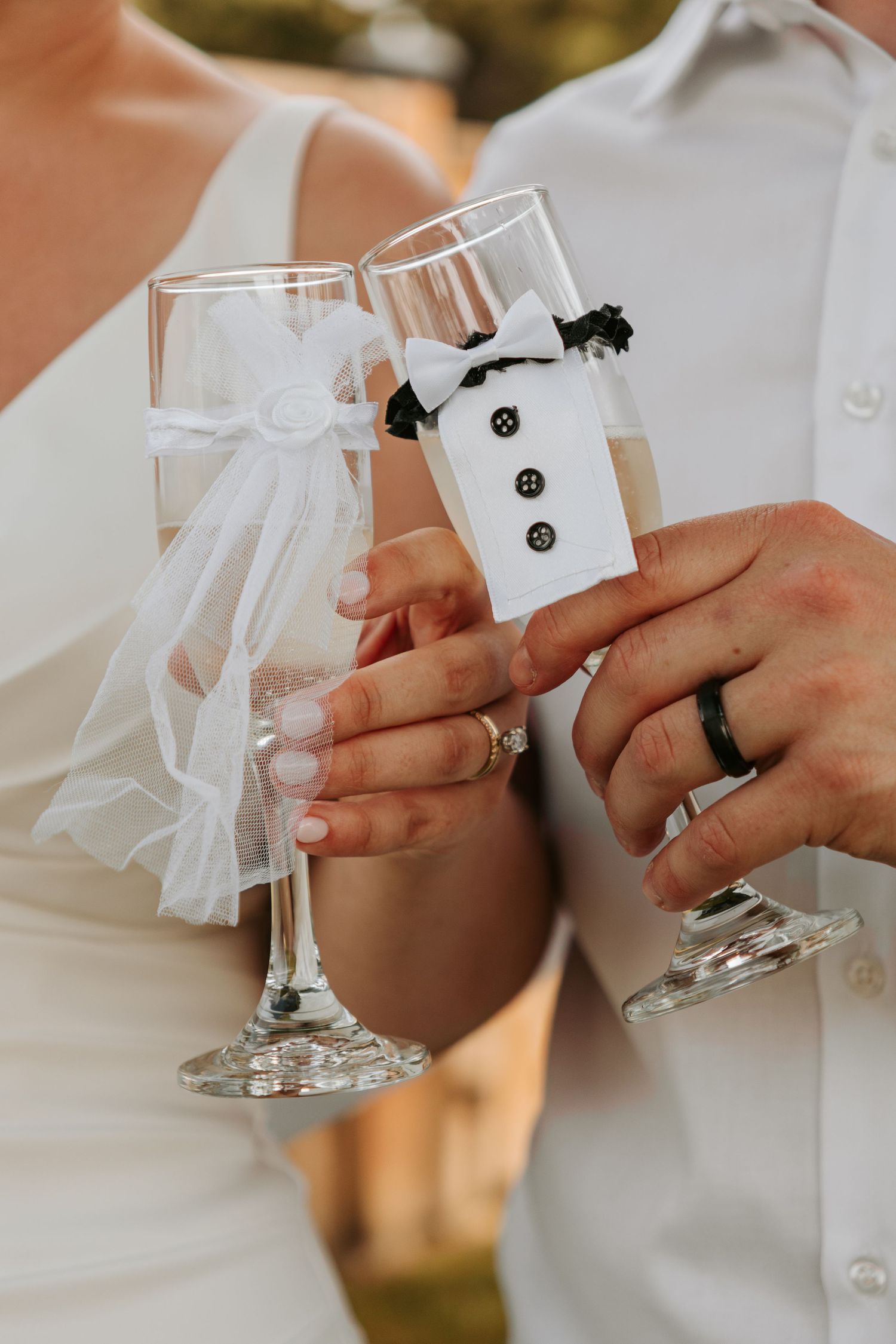 Detail shot of champagne glasses decorated with miniature tuxedo designs at a wedding celebration.
