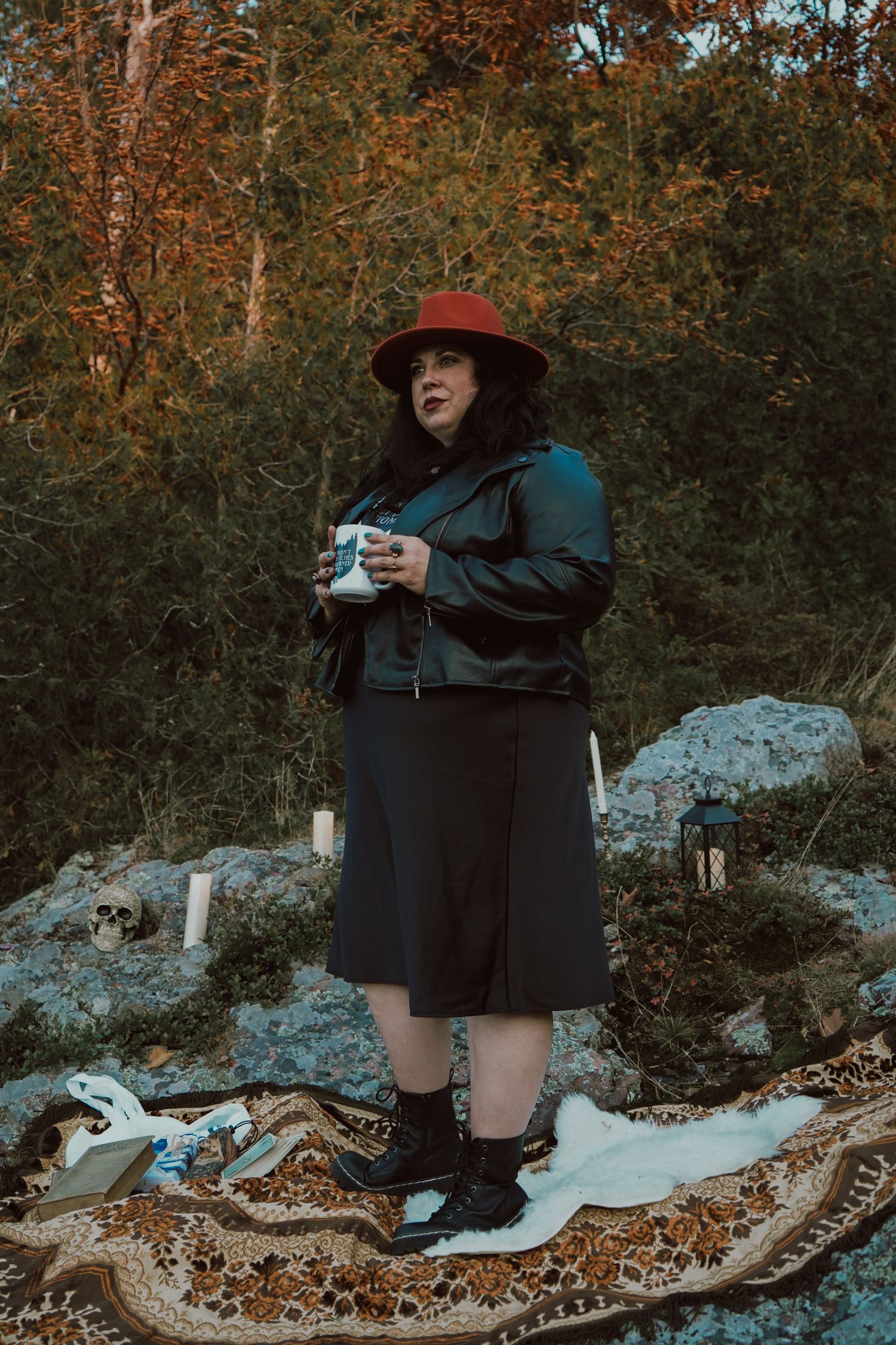 Person in black outfit and red hat posing on rocky terrain with autumn foliage.