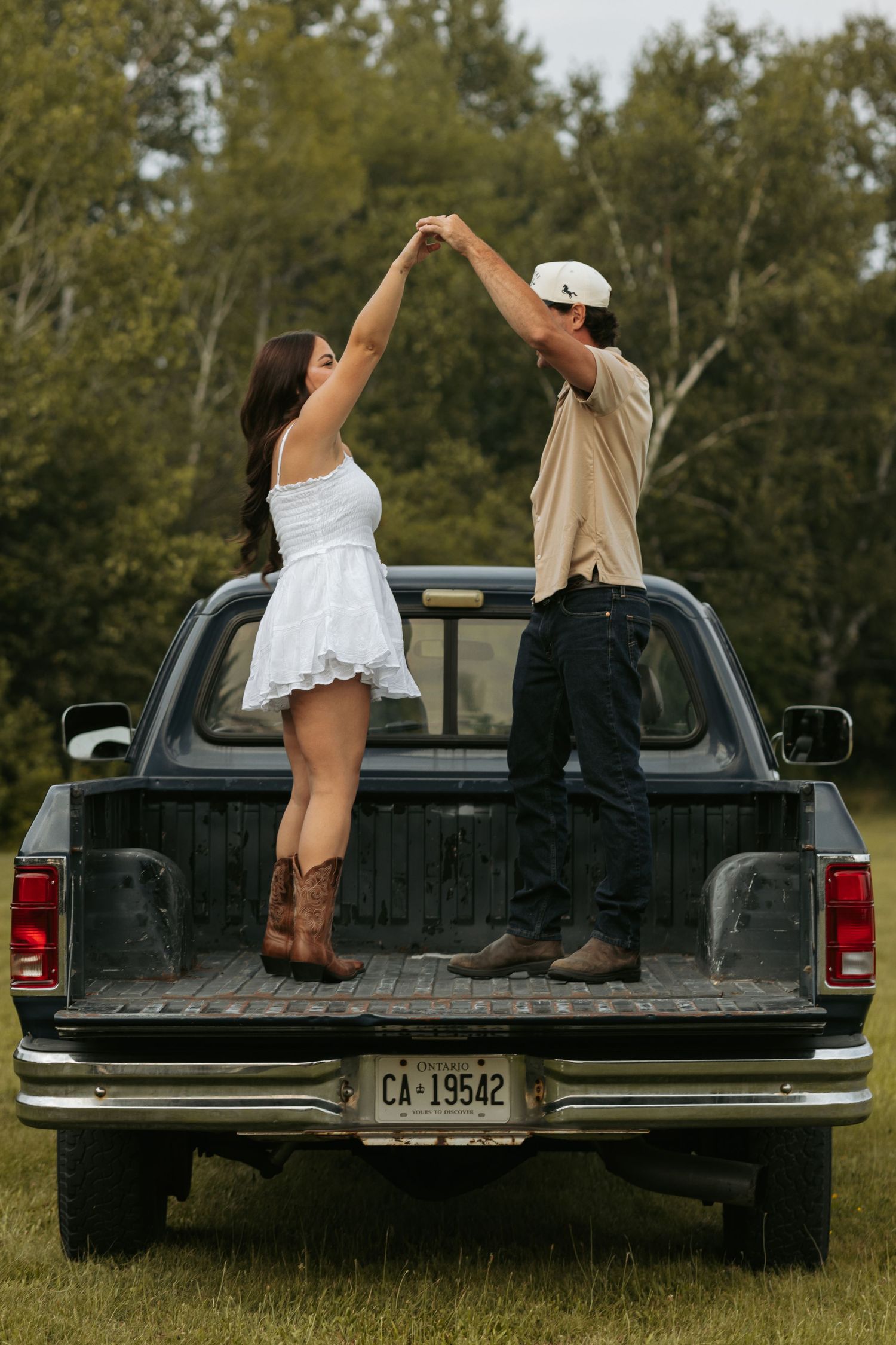 A couple sits playfully in the bed of a black pickup truck.