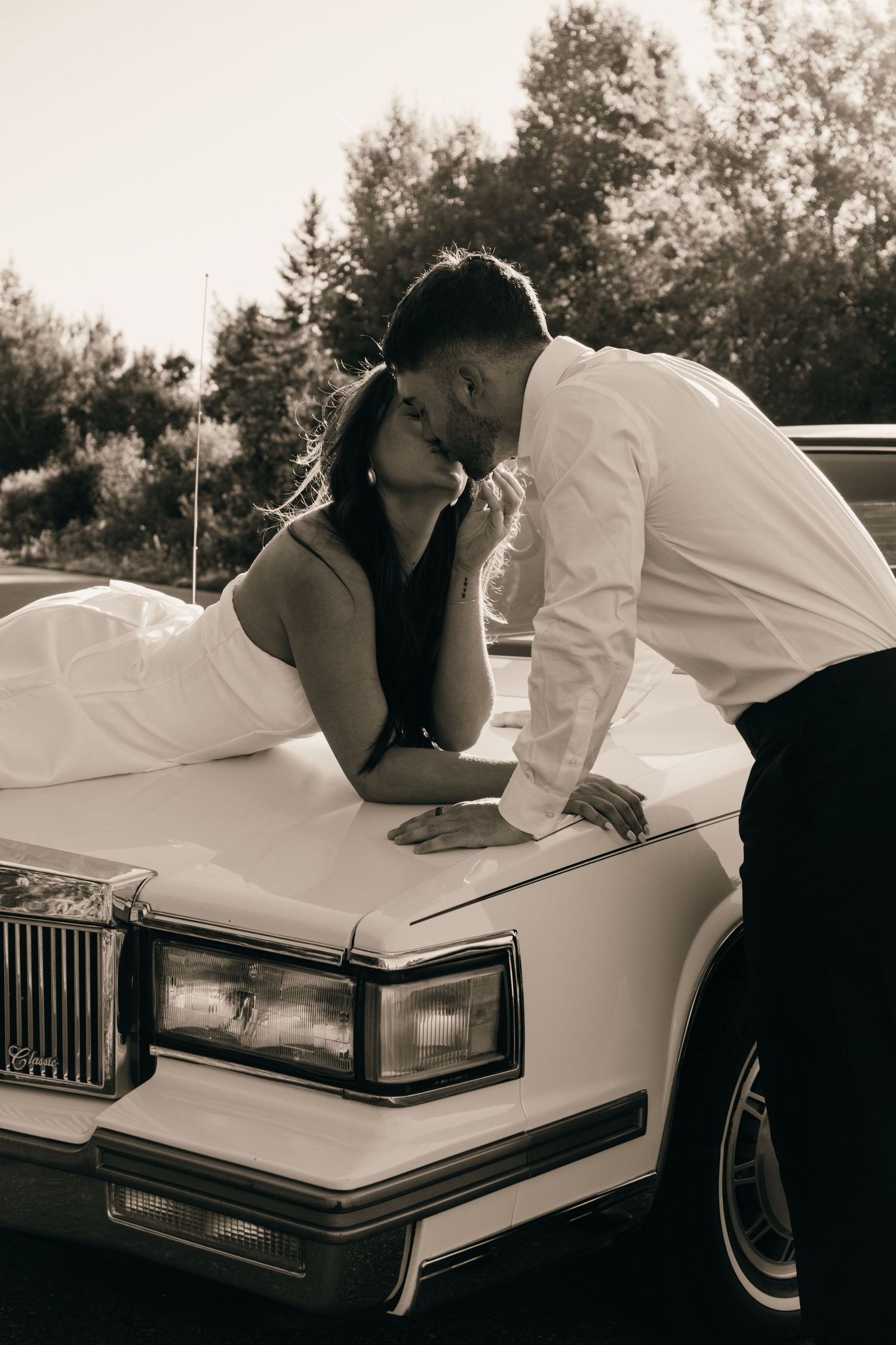 Artistic black and white photo of a couple leaning on a vintage car.