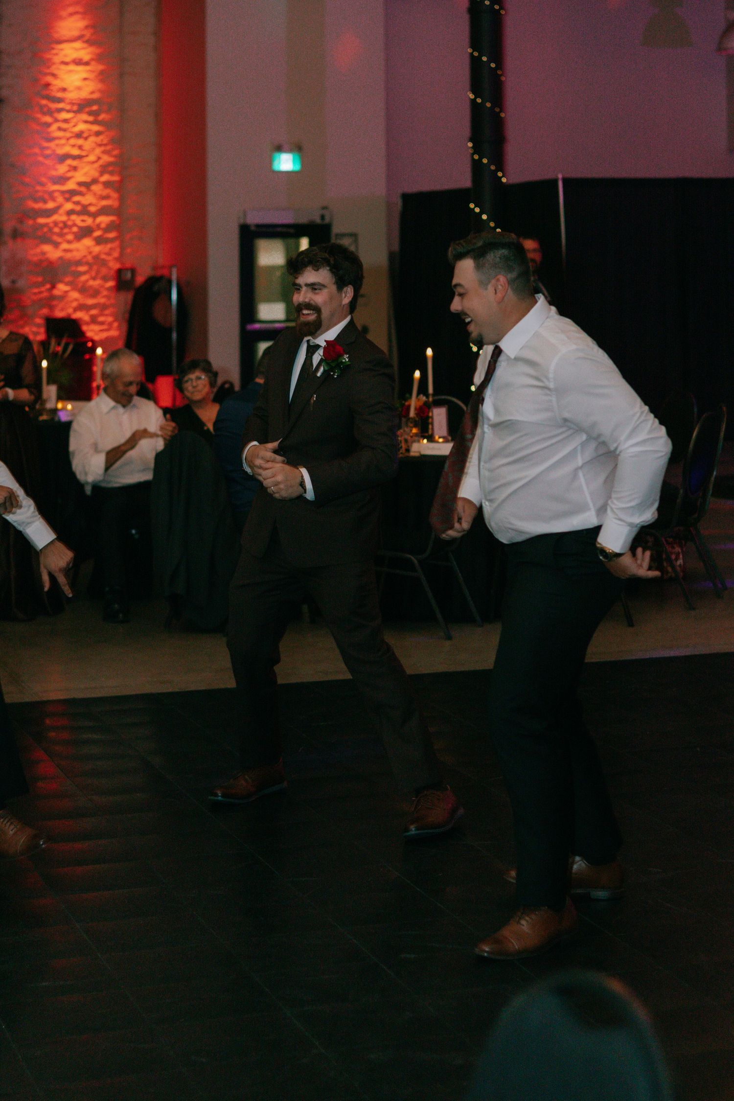 Wedding guests dancing together in formal attire at an indoor reception venue.