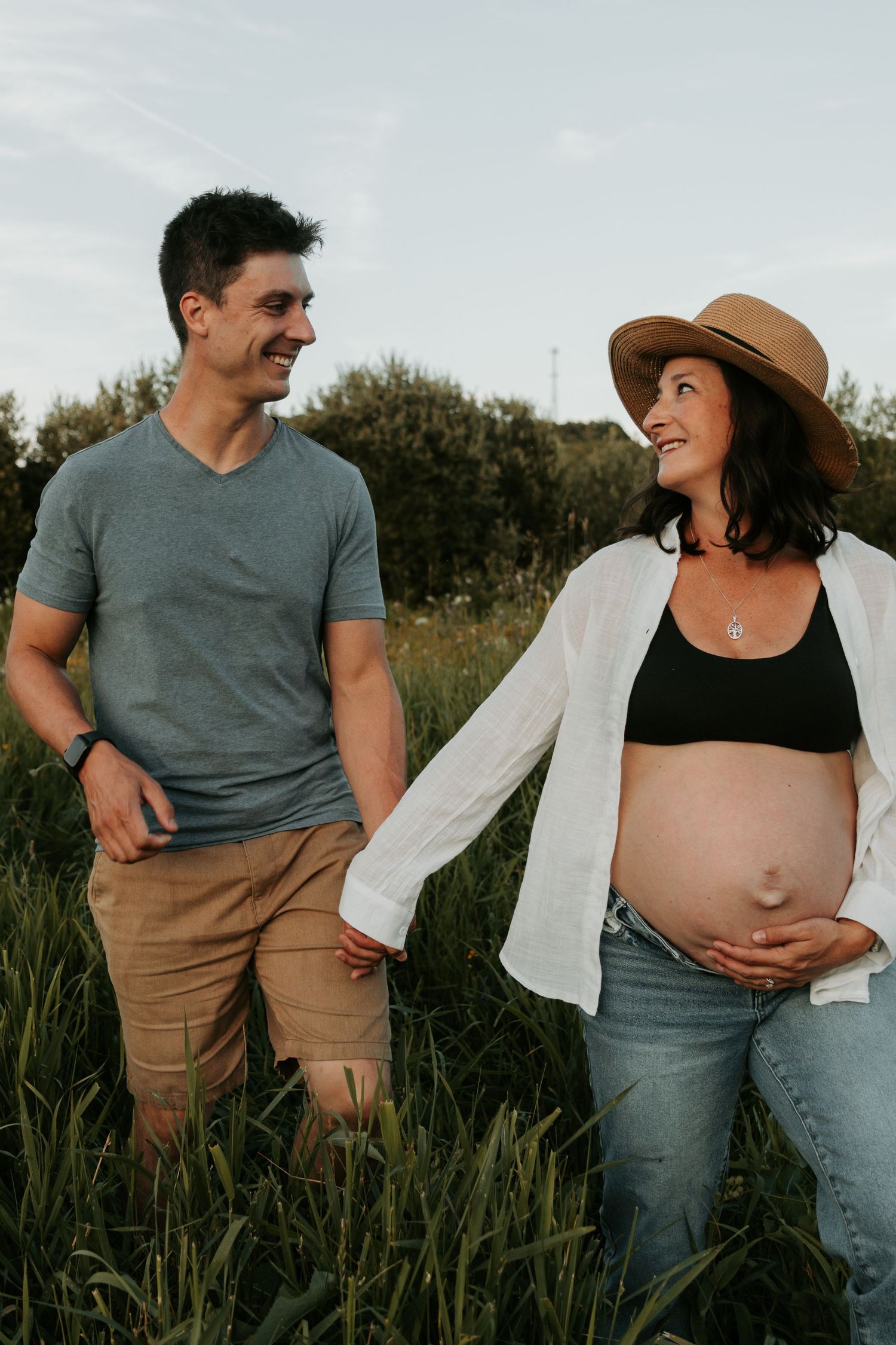 Maternity photo session in a field with couple in casual attire.