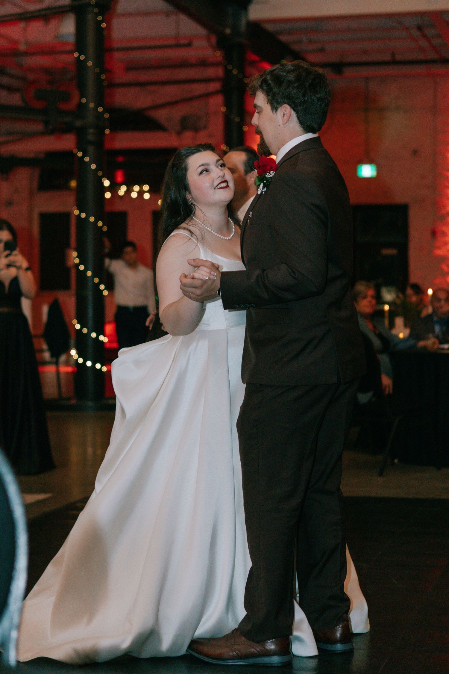 A couple shares a romantic dance moment at their wedding reception under twinkling lights.