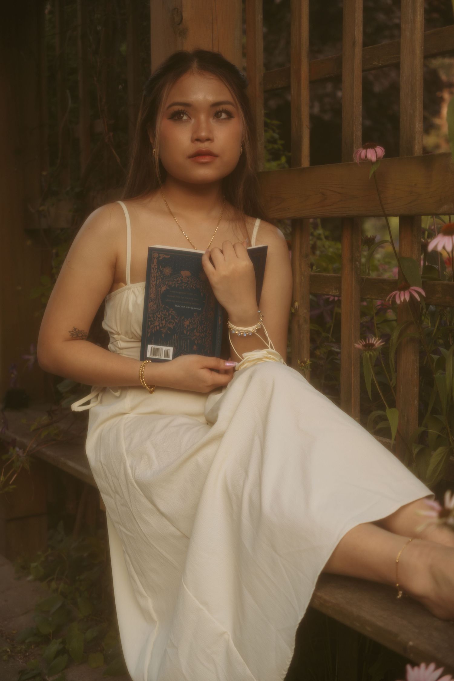 A vintage-inspired portrait of someone in white dress sitting on wooden bench with a book.