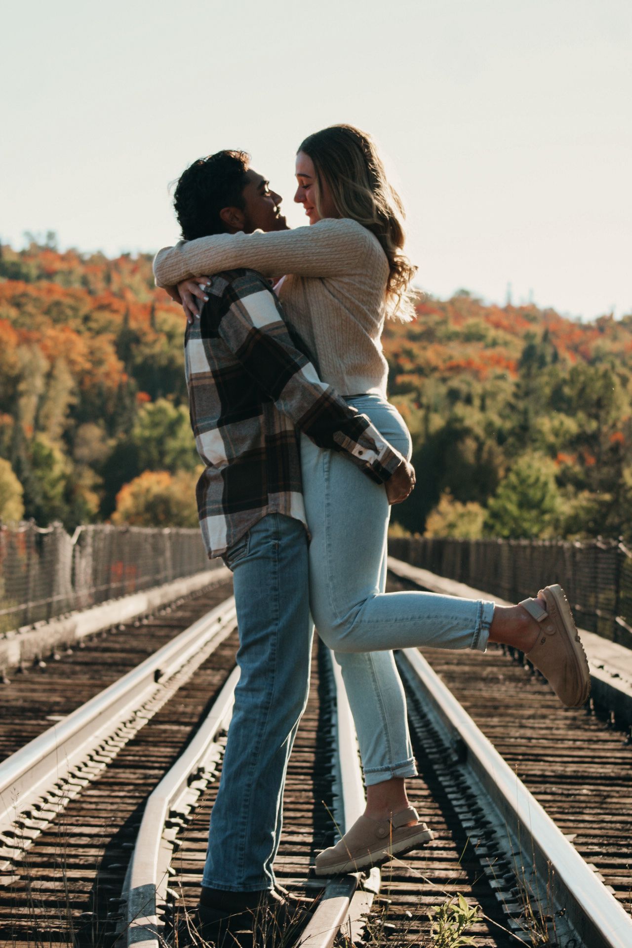 Romantic couple embracing on railroad tracks during autumn sunset.