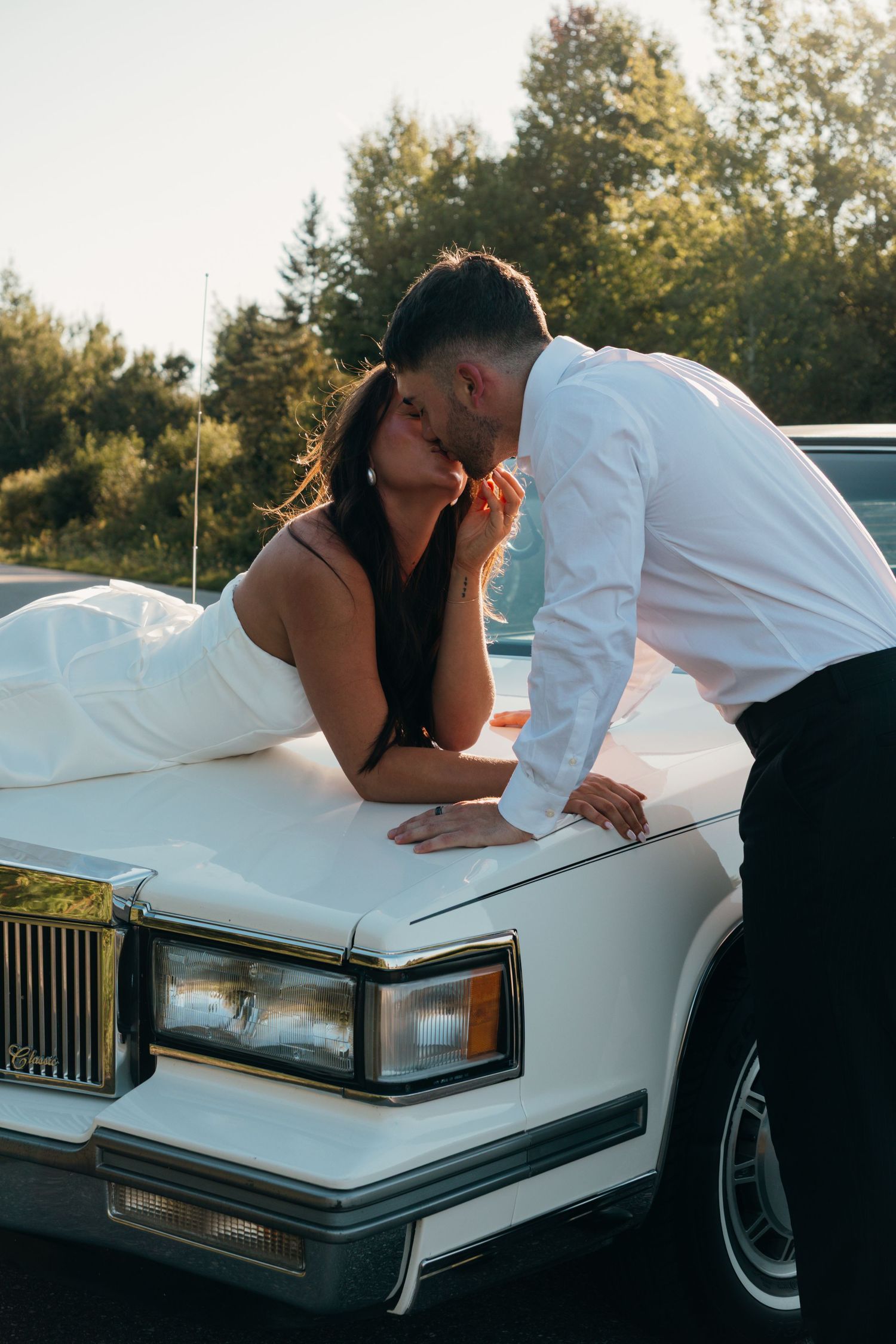 Romantic couple shares tender moment on hood of vintage white car.