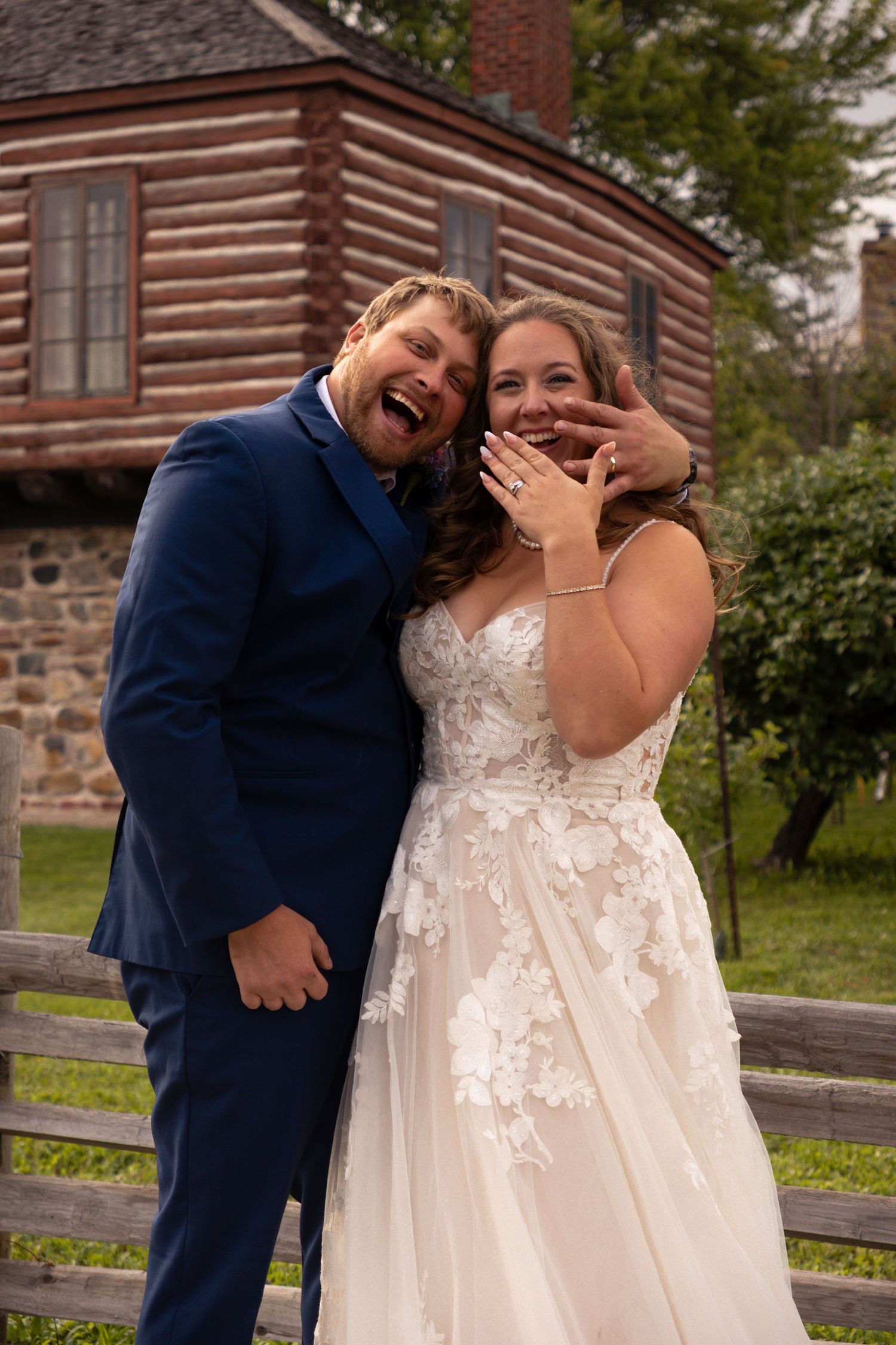 A couple shares laughter and joy in front of a rustic log cabin on their wedding day.