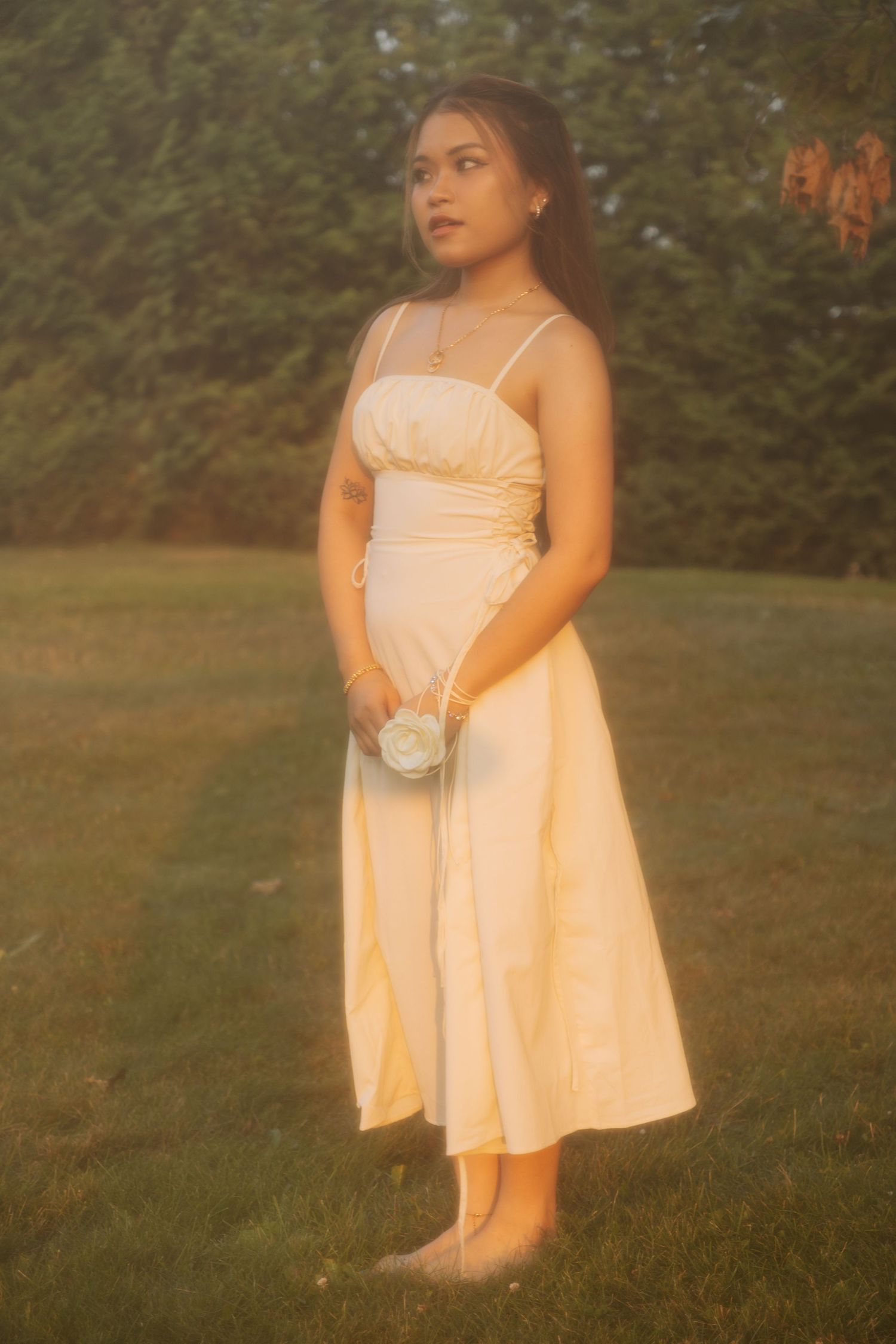 A romantic garden photo of someone in an elegant white dress holding a small purse at sunset.