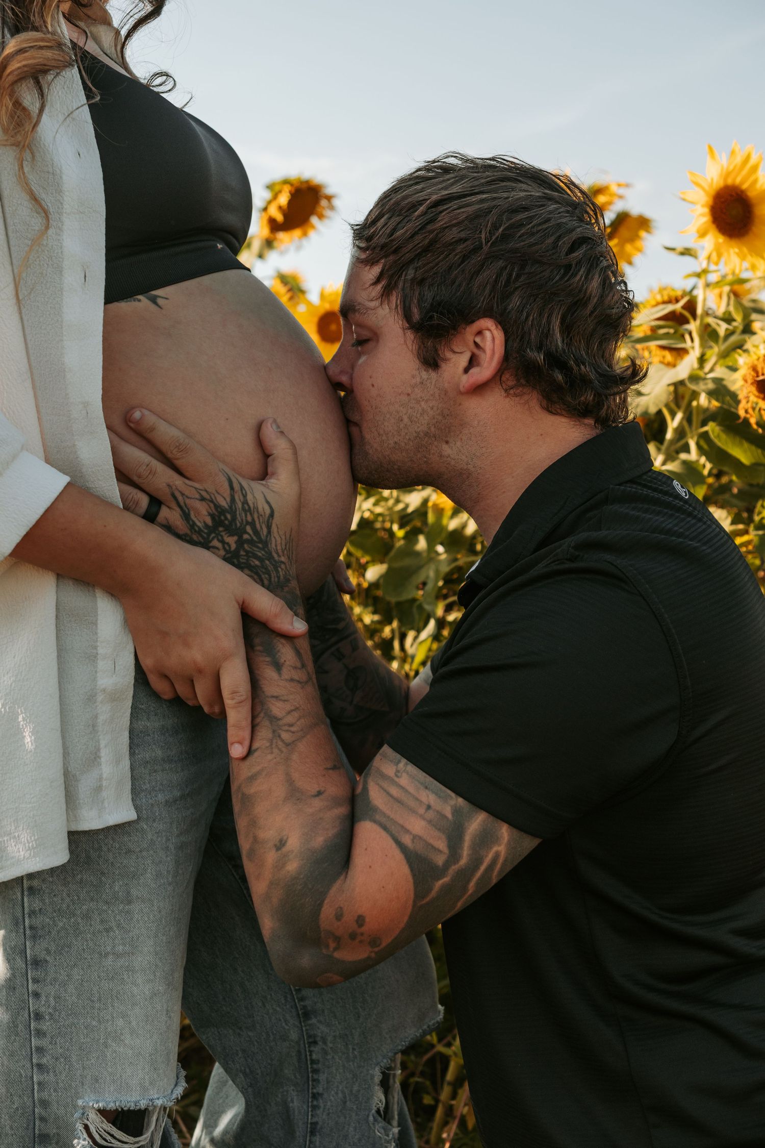 Intimate pregnancy announcement moment captured in a sunflower field at dusk.