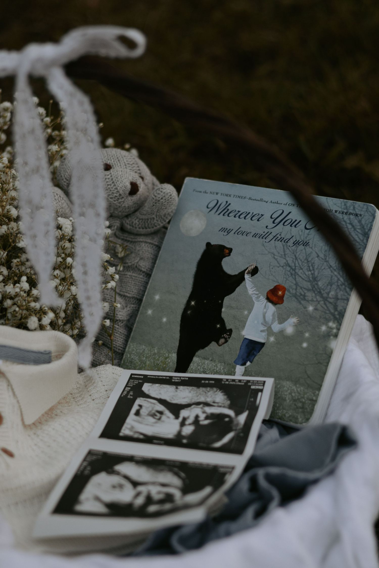Pregnancy announcement items arranged with ultrasound photos and soft textiles.