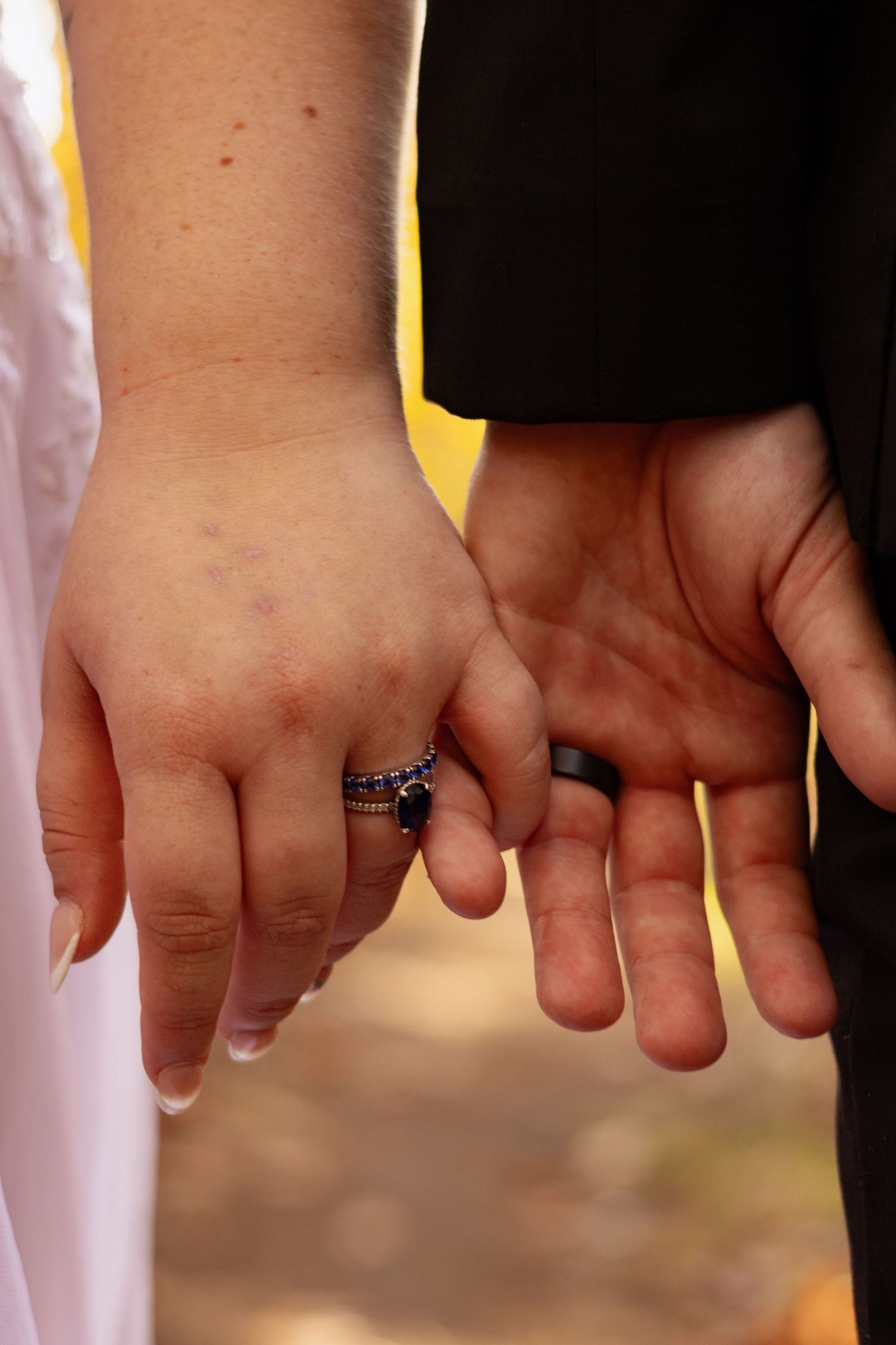 Close-up of bride and groom's hands with wedding rings against autumn backdrop.