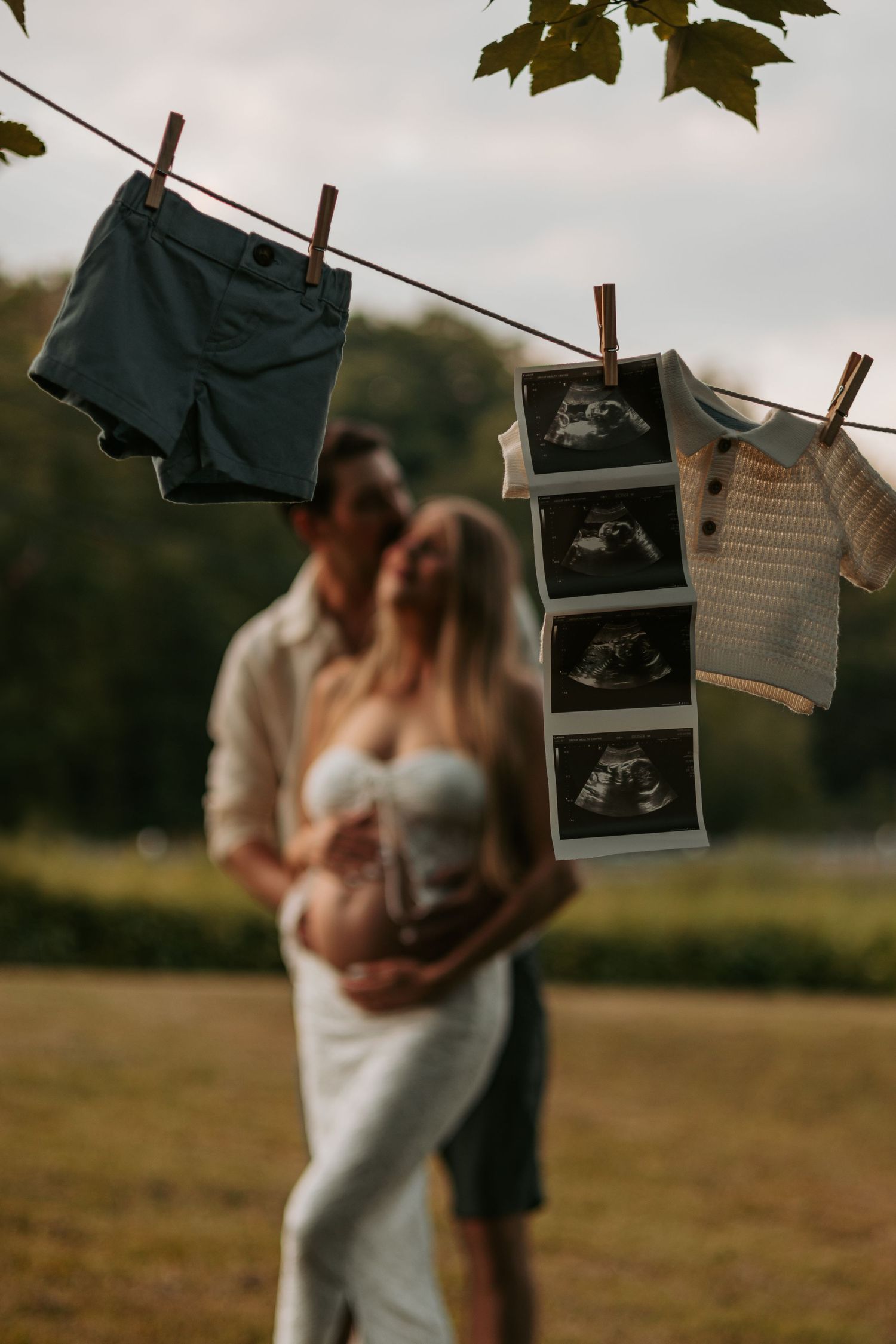 Pregnancy announcement photos hanging on a clothesline with ultrasound images and couple embracing in background.