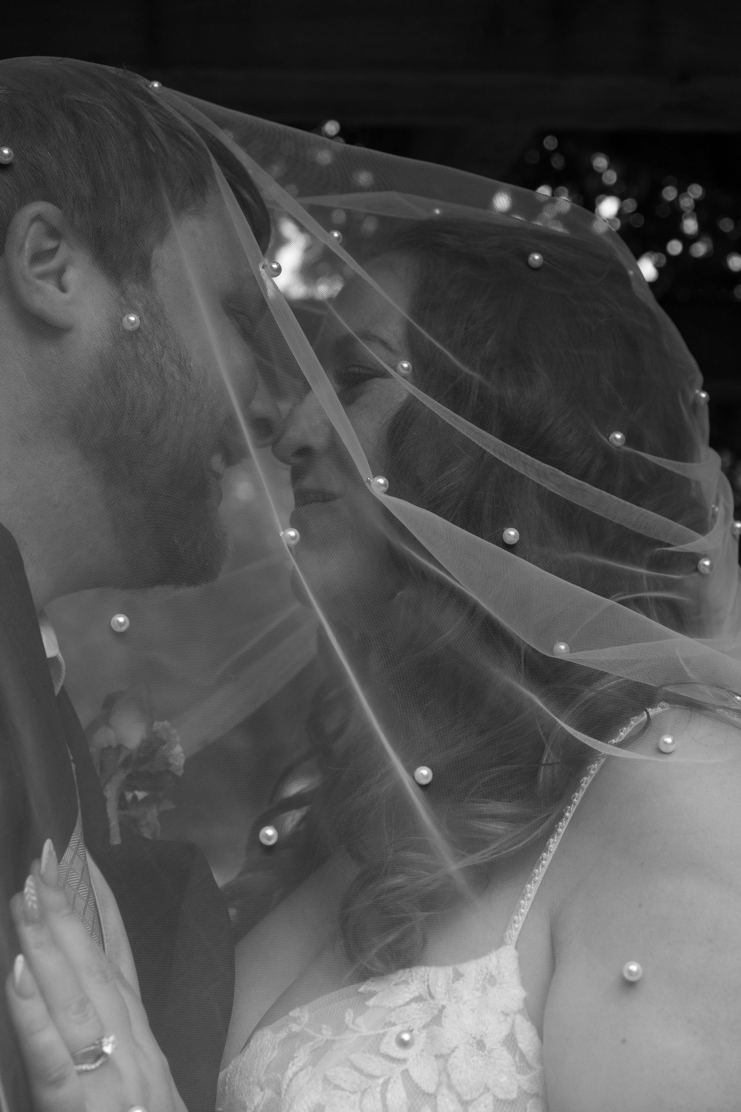 A romantic black and white photo series showing a couple sharing a kiss under a delicate veil with pearl details.