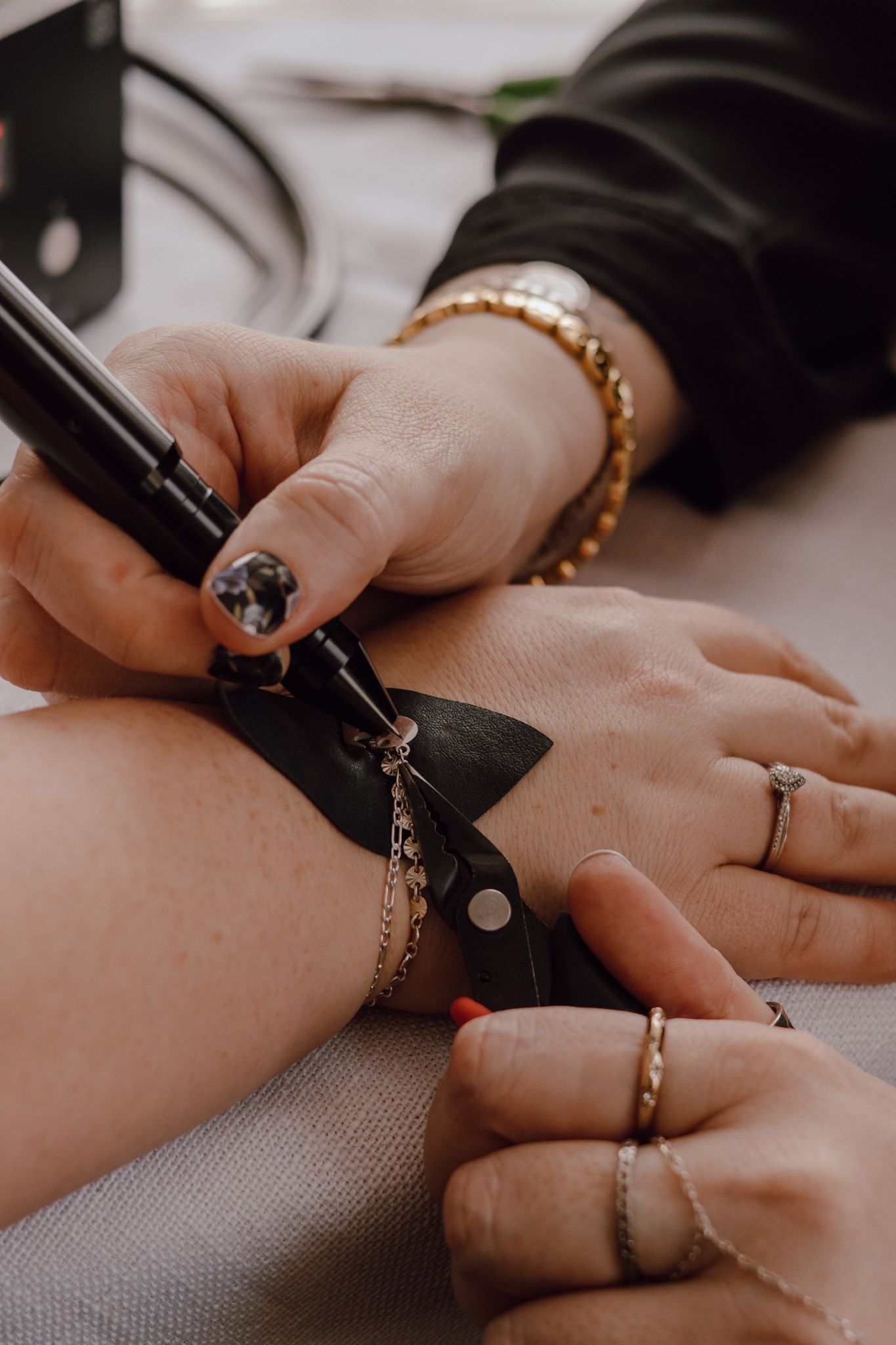 Close-up of hands measuring delicate jewelry chains with a ruler on a gray surface.