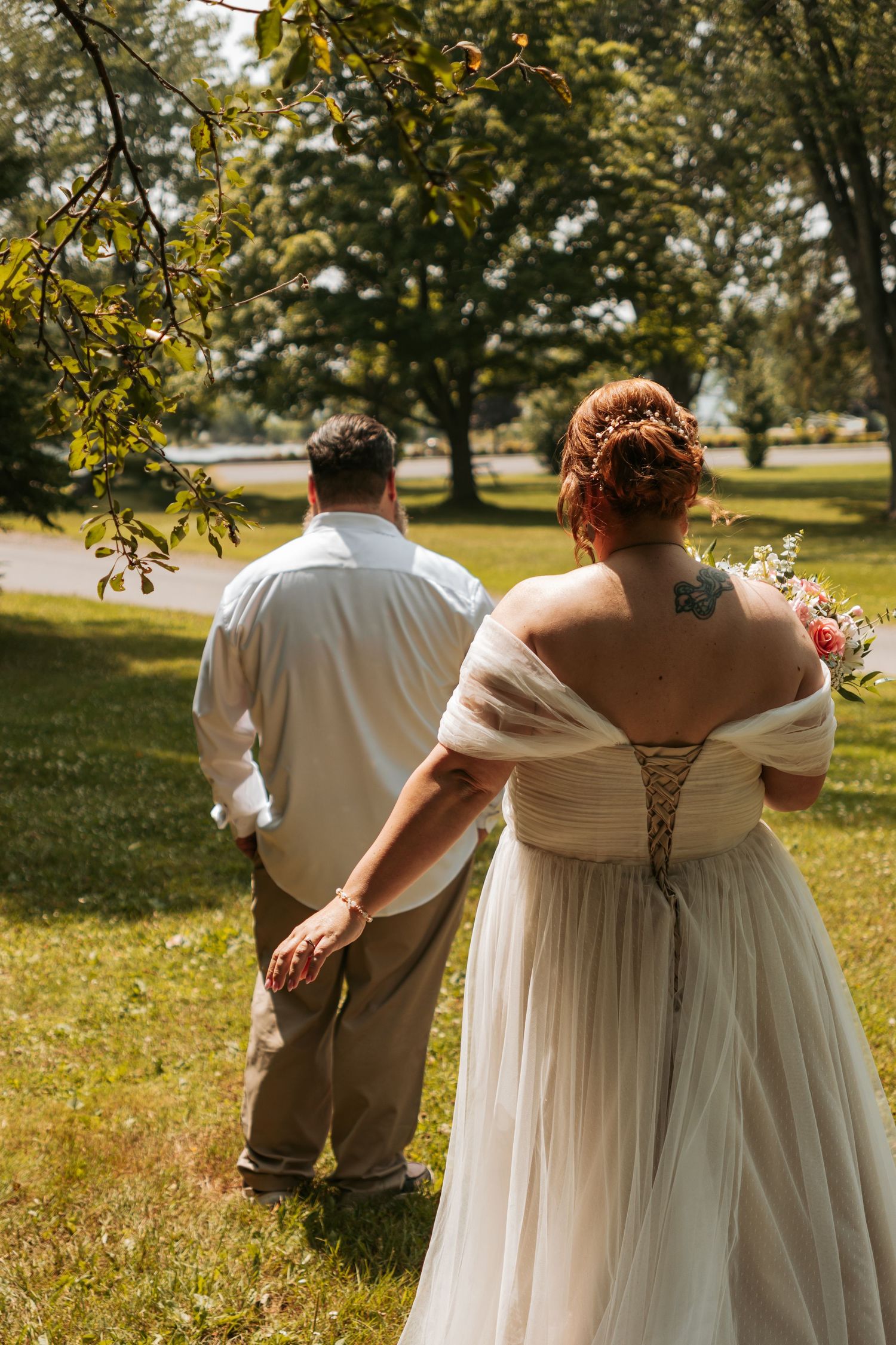 A candid wedding photo showing couple from behind walking through a sunlit park.