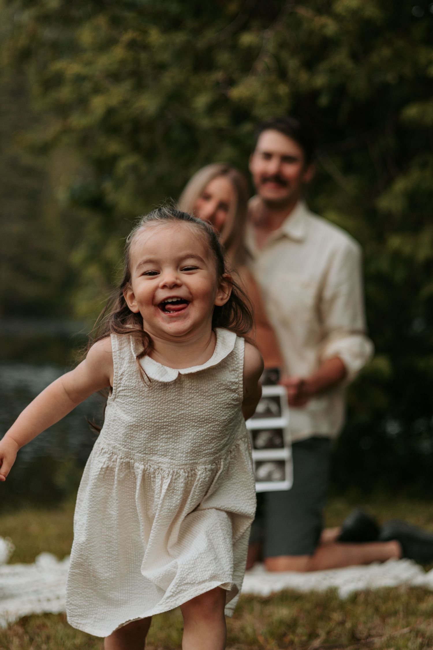 Young child in white dress laughing and playing outdoors.