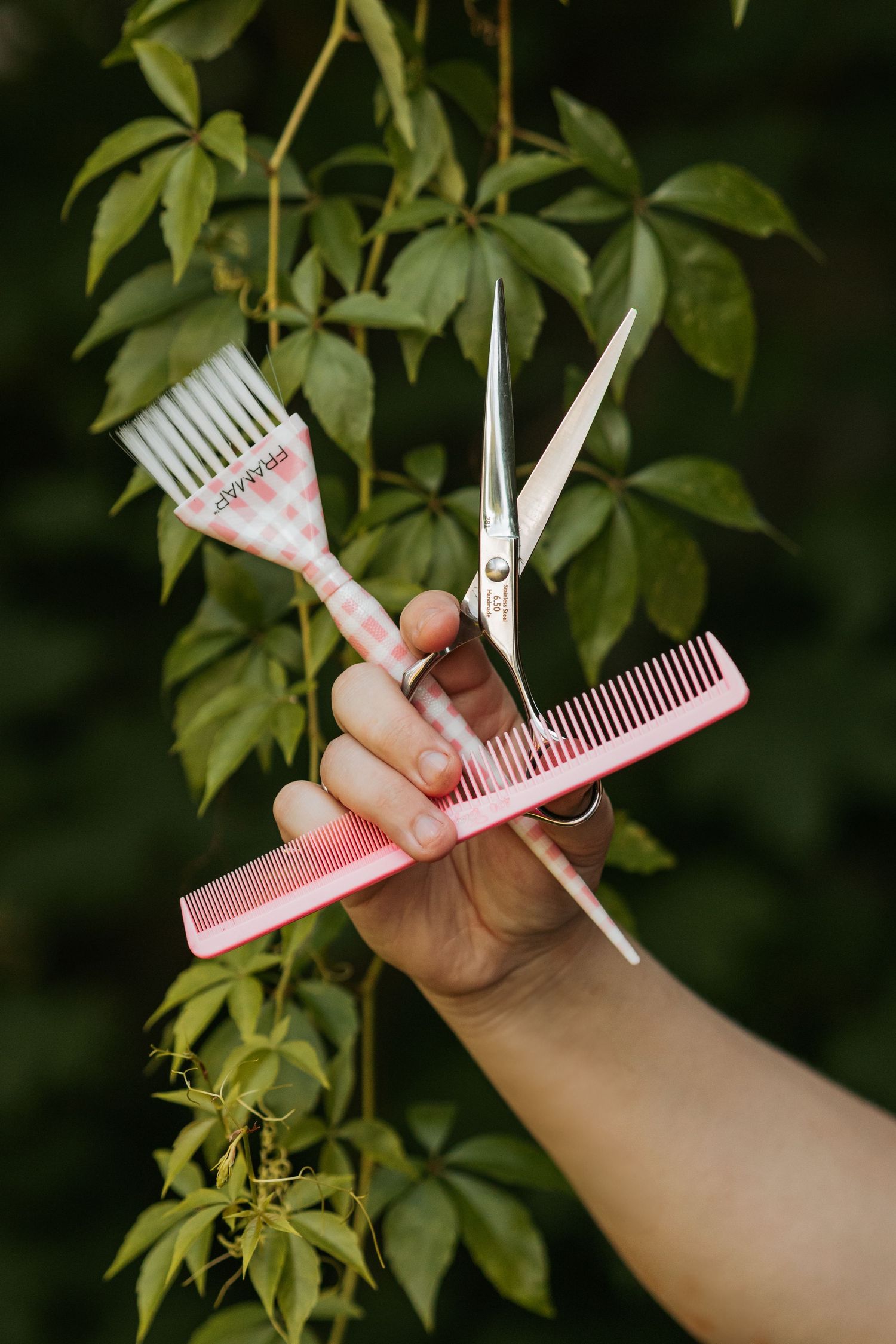 Hand holding pink hair styling combs against green foliage background.