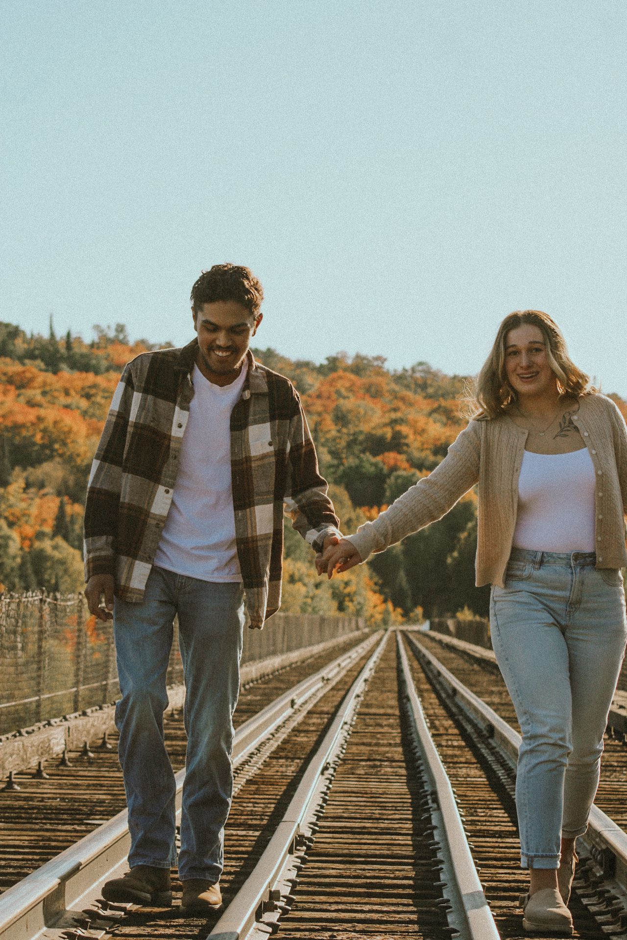 Casual couple walking and laughing together on train tracks during fall.