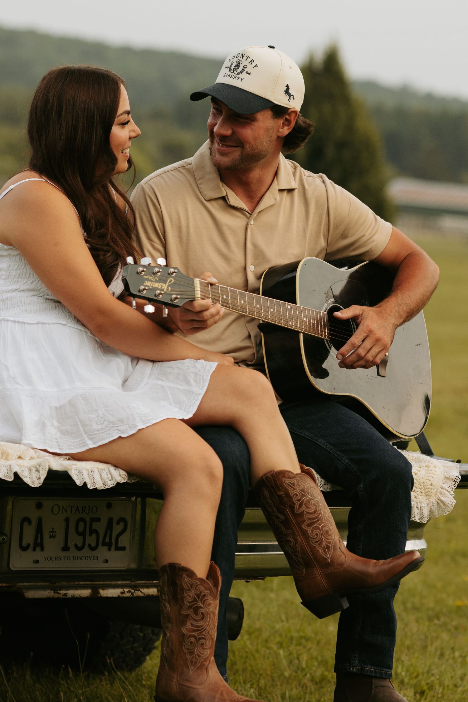 A couple sits together with an acoustic guitar in a grassy field.