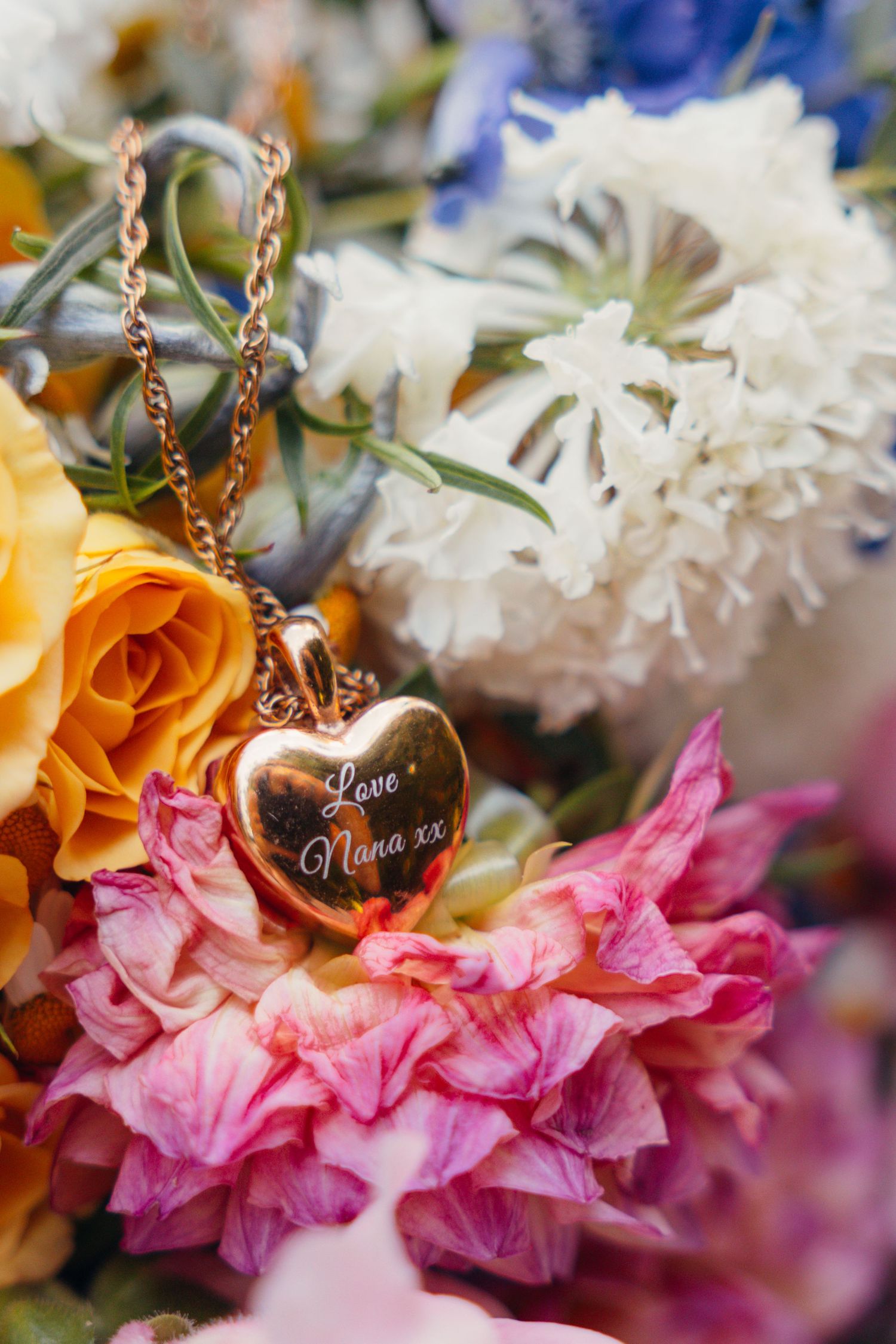 Delicate heart pendant on chain surrounded by pink and orange floral arrangements.