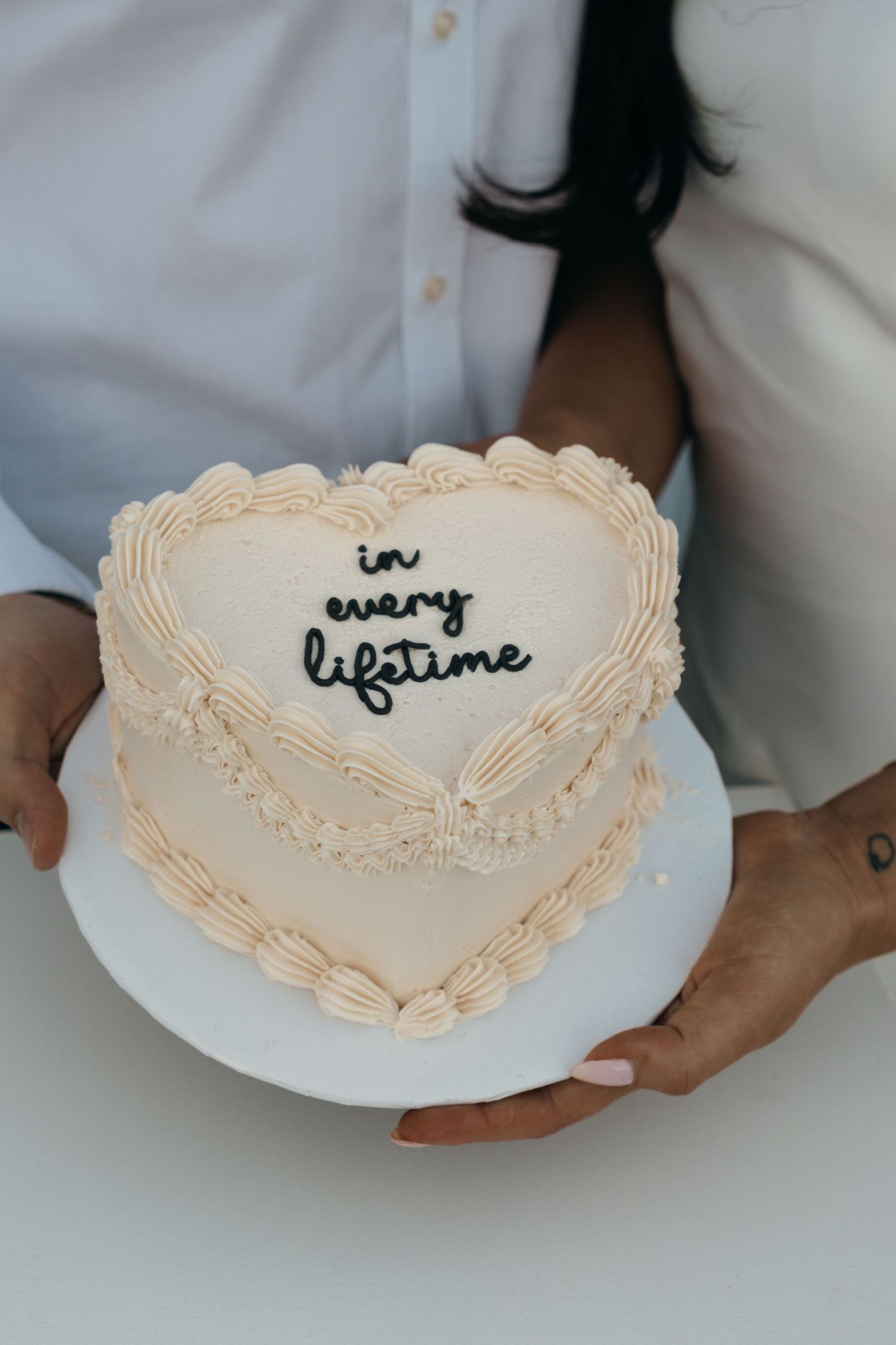 Heart-shaped cake with delicate piped frosting border displayed on white plate.