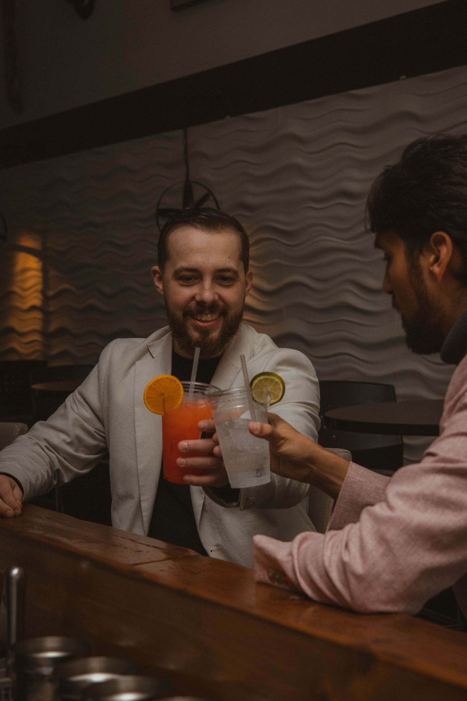 Two people enjoying cocktails at a dimly lit bar with textured walls.