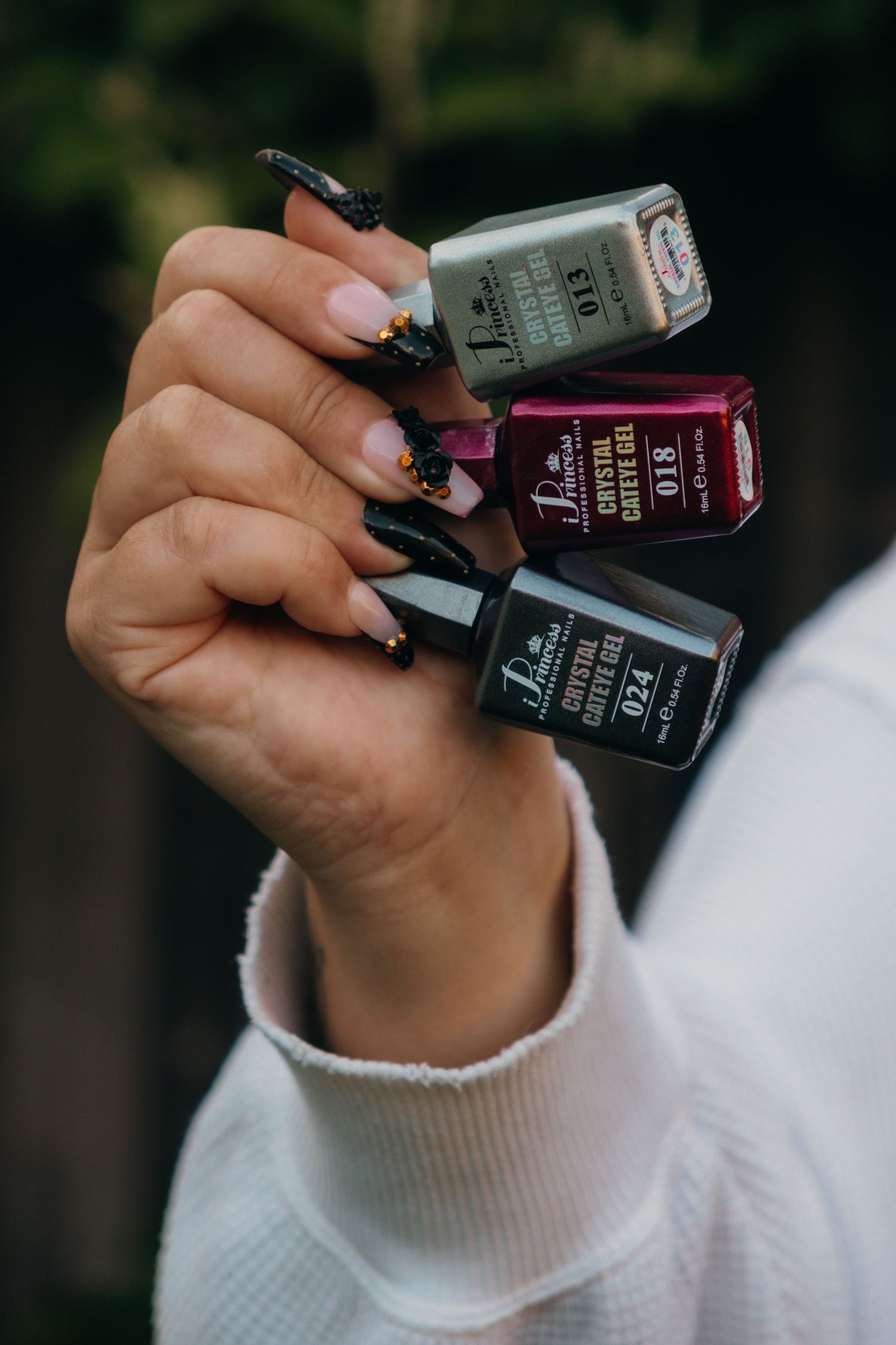 Several bottles of dark nail polish held in hand against a black background.
