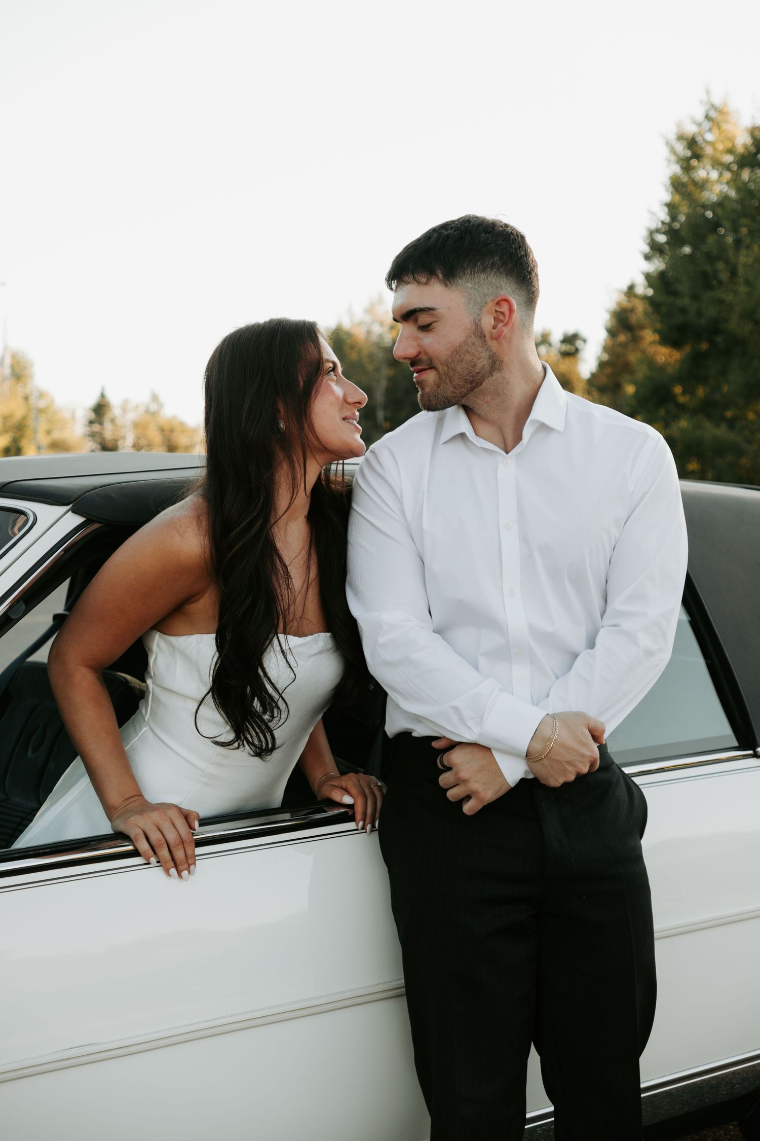 Romantic couple in black and white outfits sharing intimate moments by a vintage car.