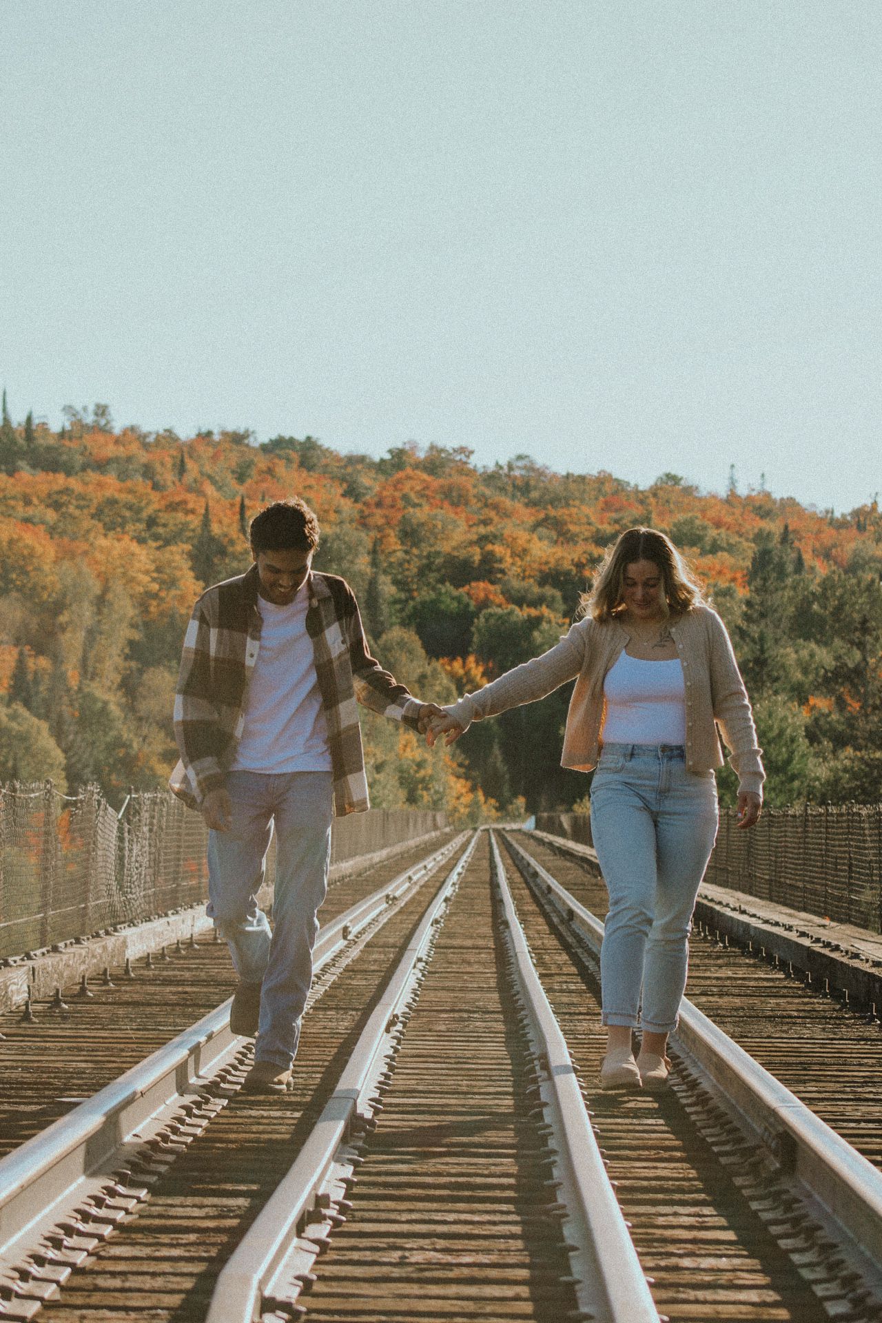 Two people walking intimately along train tracks with fall colors in background.