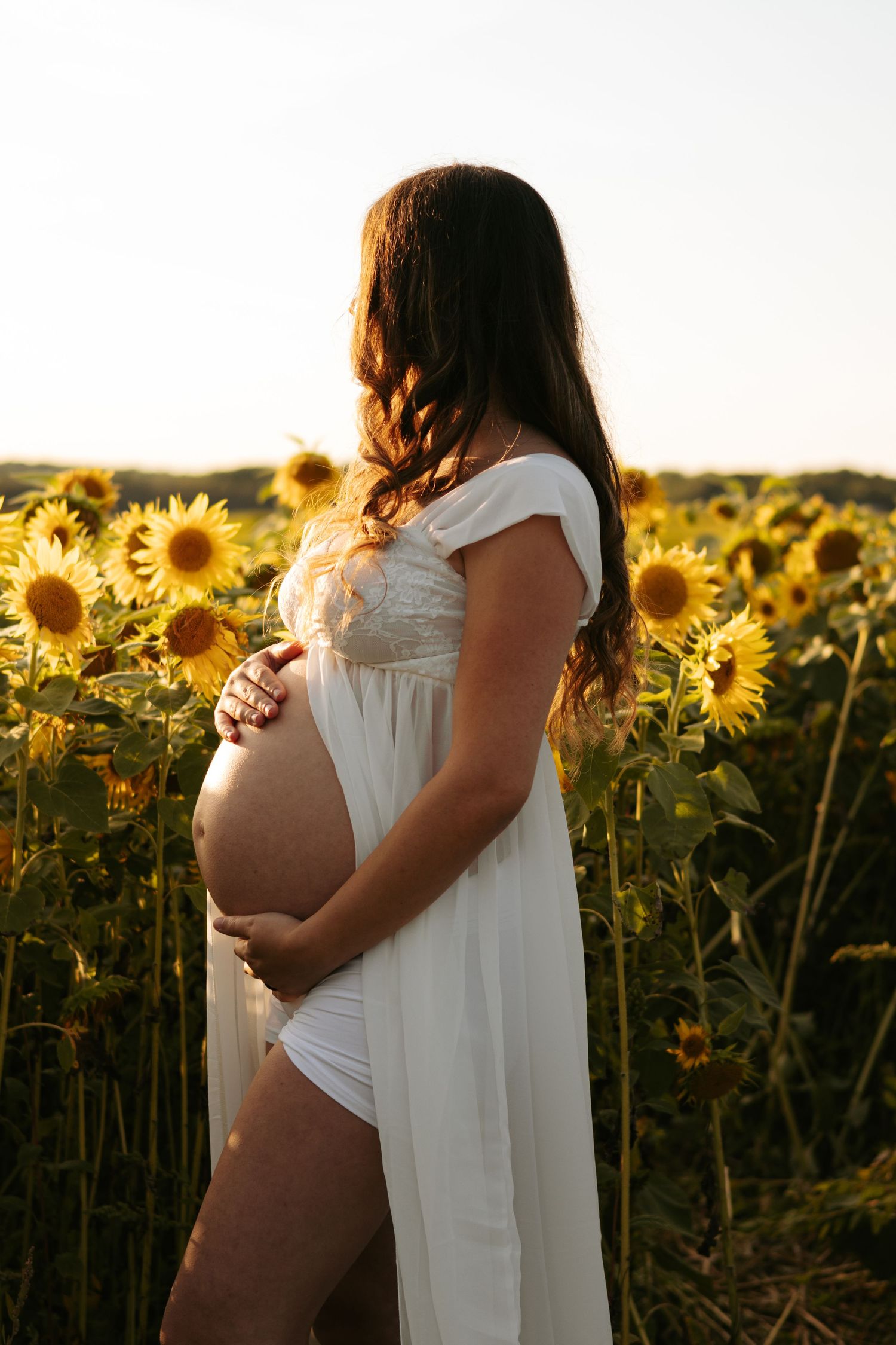 Side view maternity portraits in sunflower field during golden hour.
