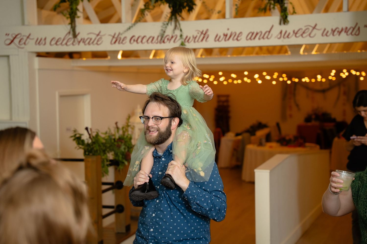 A young wedding guest rides on her father's shoulders during the dance party of a queer wedding in the Shenandoah Valley