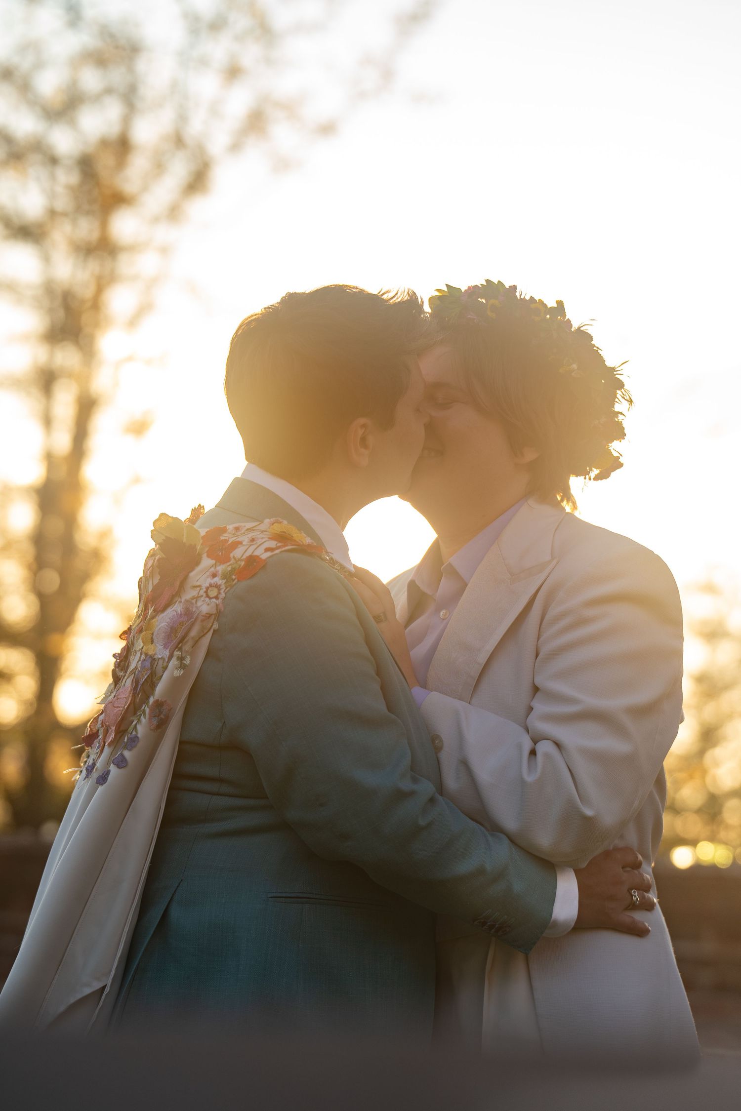 Queer couple in a white & blue suits share a kiss in a dreamy sunset newlywed portrait in the gardens of a Richmond Virginia museum