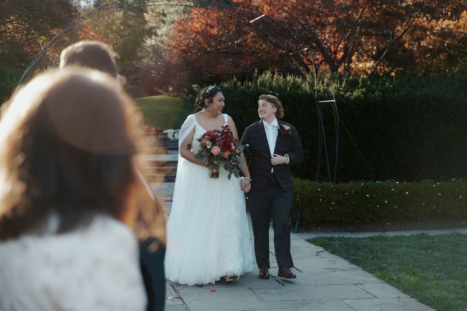 LQBTQ bride in white wedding dress walks down the aisle next to her partner in a suit at their fall wedding in Tacoma Park Maryland.