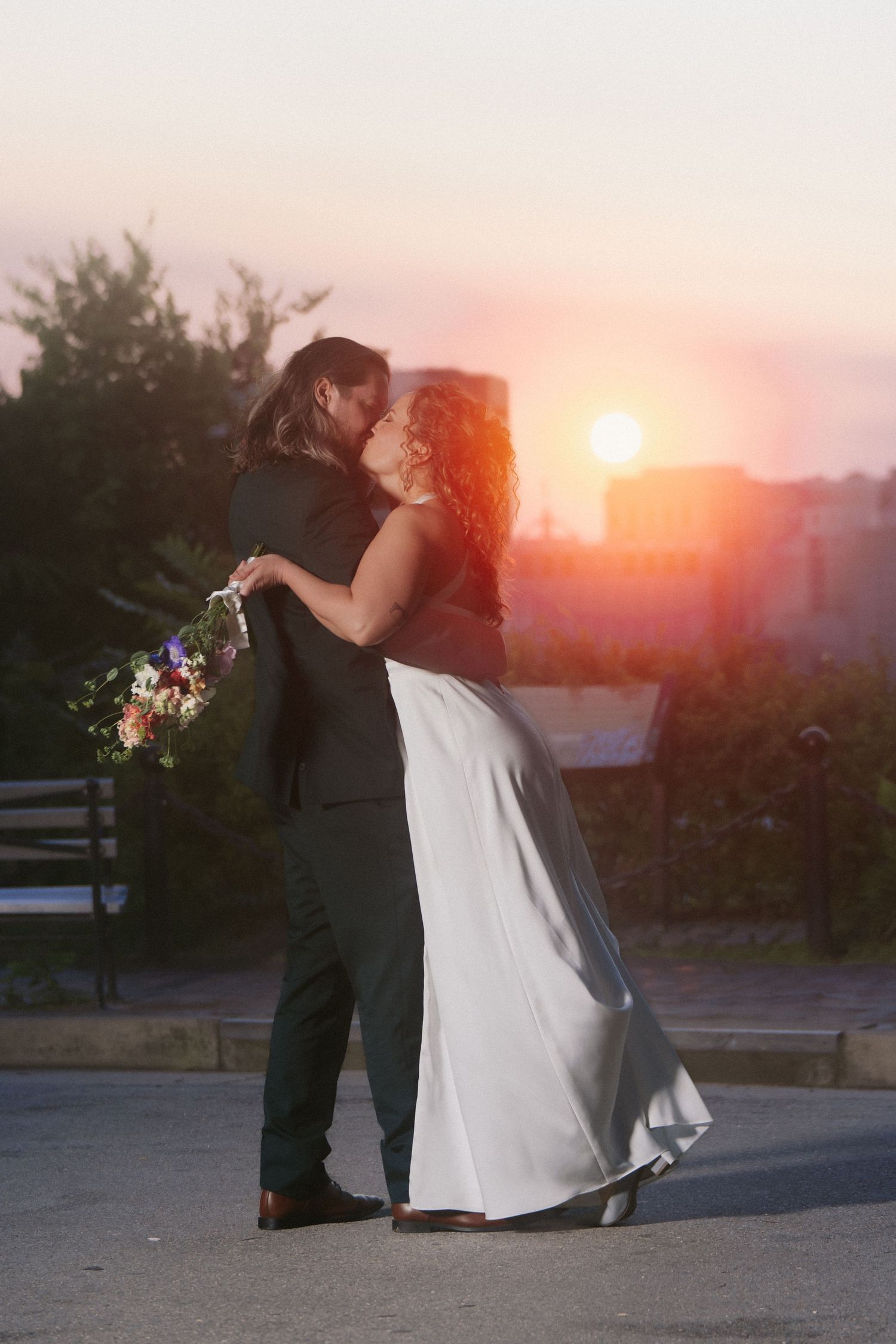 Dreamy landscape portrait of bride in classic wedding dress kissing her groom against the sunset skyline of Richmond Virginia