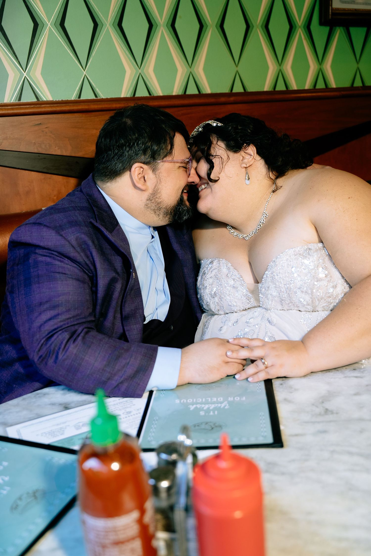 Couple kisses sitting at table in quirky cool-girl wedding aesthetic newlywed photo session in Pearly's diner in Richmond Virginia