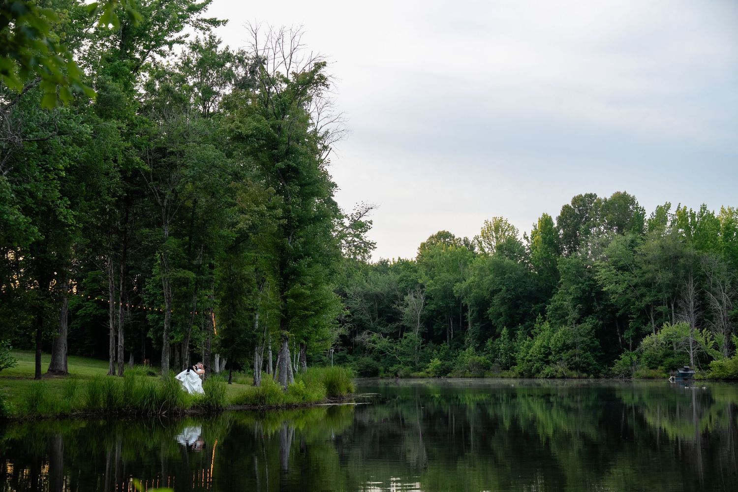 Groom dips bride in wide environmental portrait by photographer Daniel Bowler of wedding at lake outside Richmond Virginia at Avonlea Farms