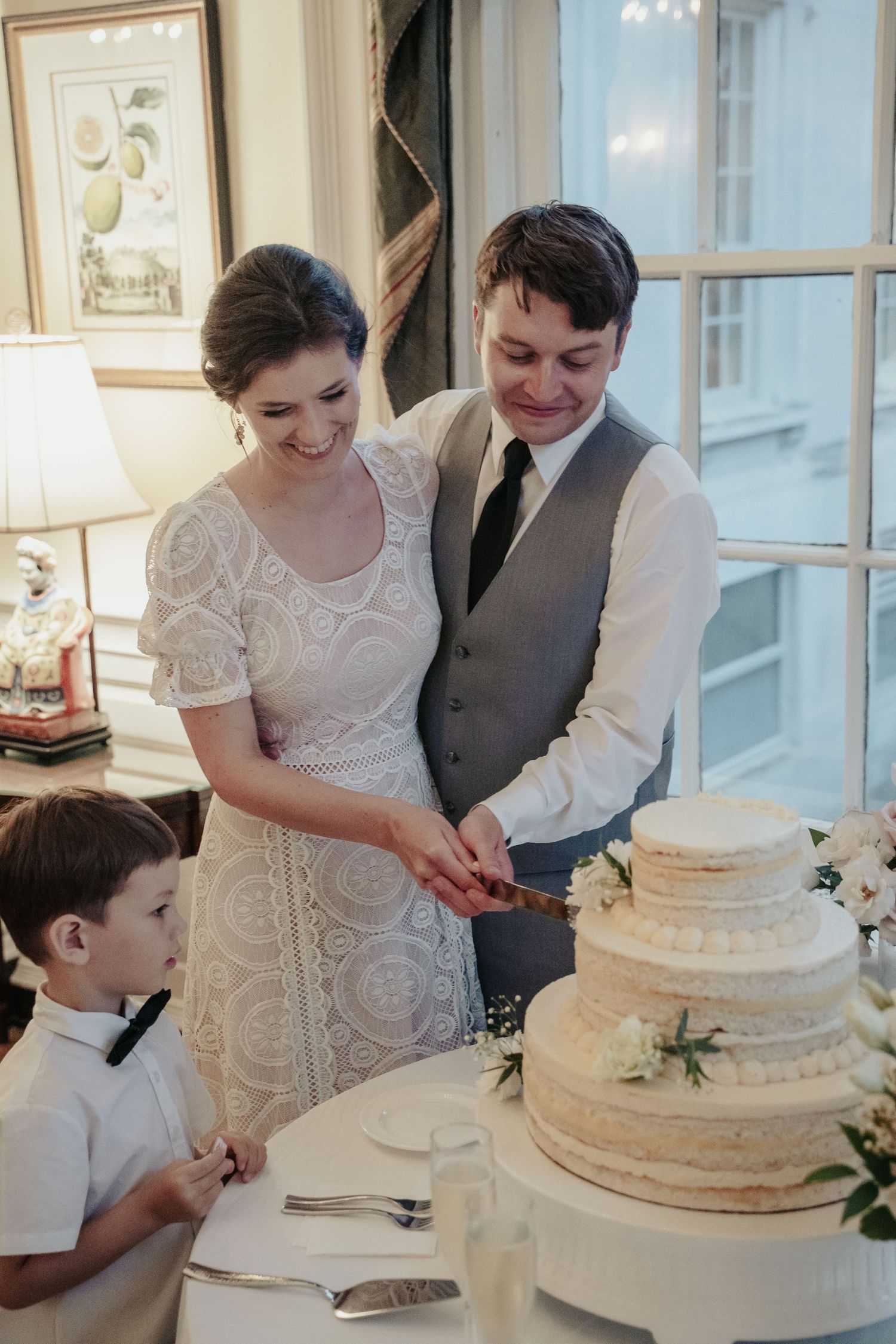 Richmond bride and groom smile while cutting their wedding cake in front of an eager young guest at the Virginia Museum of Fine Arts
