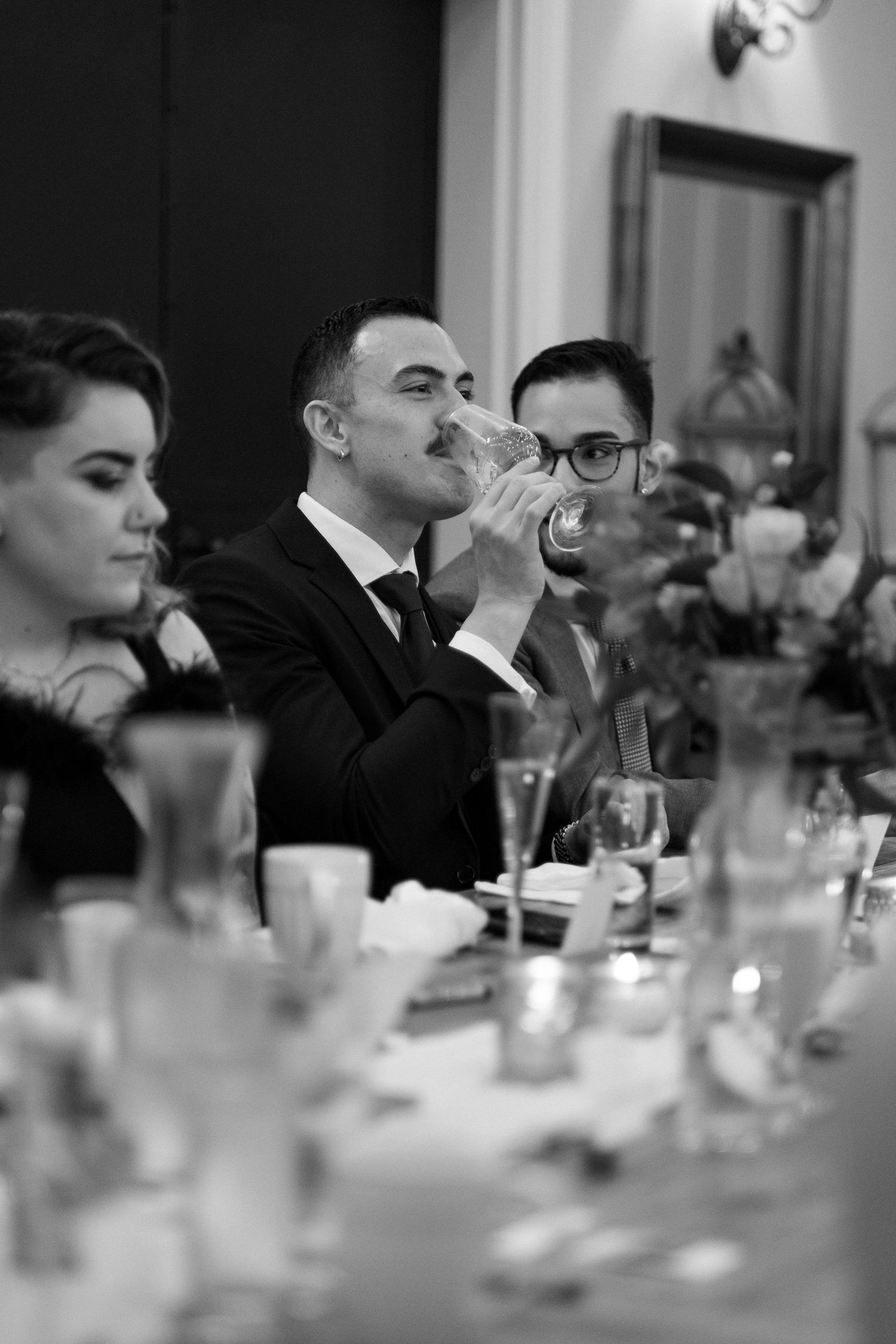 Wedding guest takes a sip of wine alongside his boyfriend  at a reception in the dining room of The Mill at Fine Creek