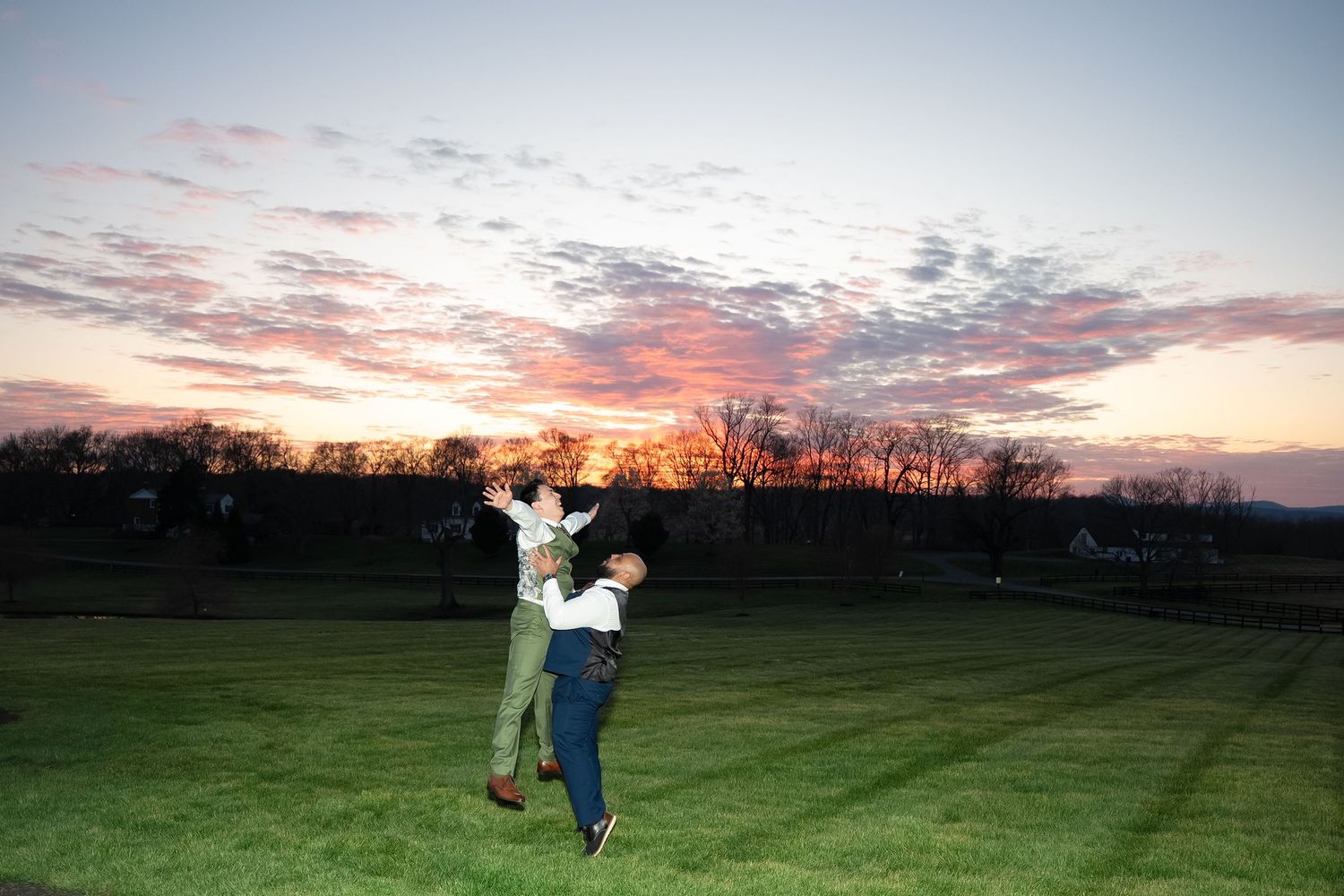 A groomsmen lifts the groomsmen up by the chest under a dramatic sunset during a wedding in central Virginia in the Blue Ridge Mountains
