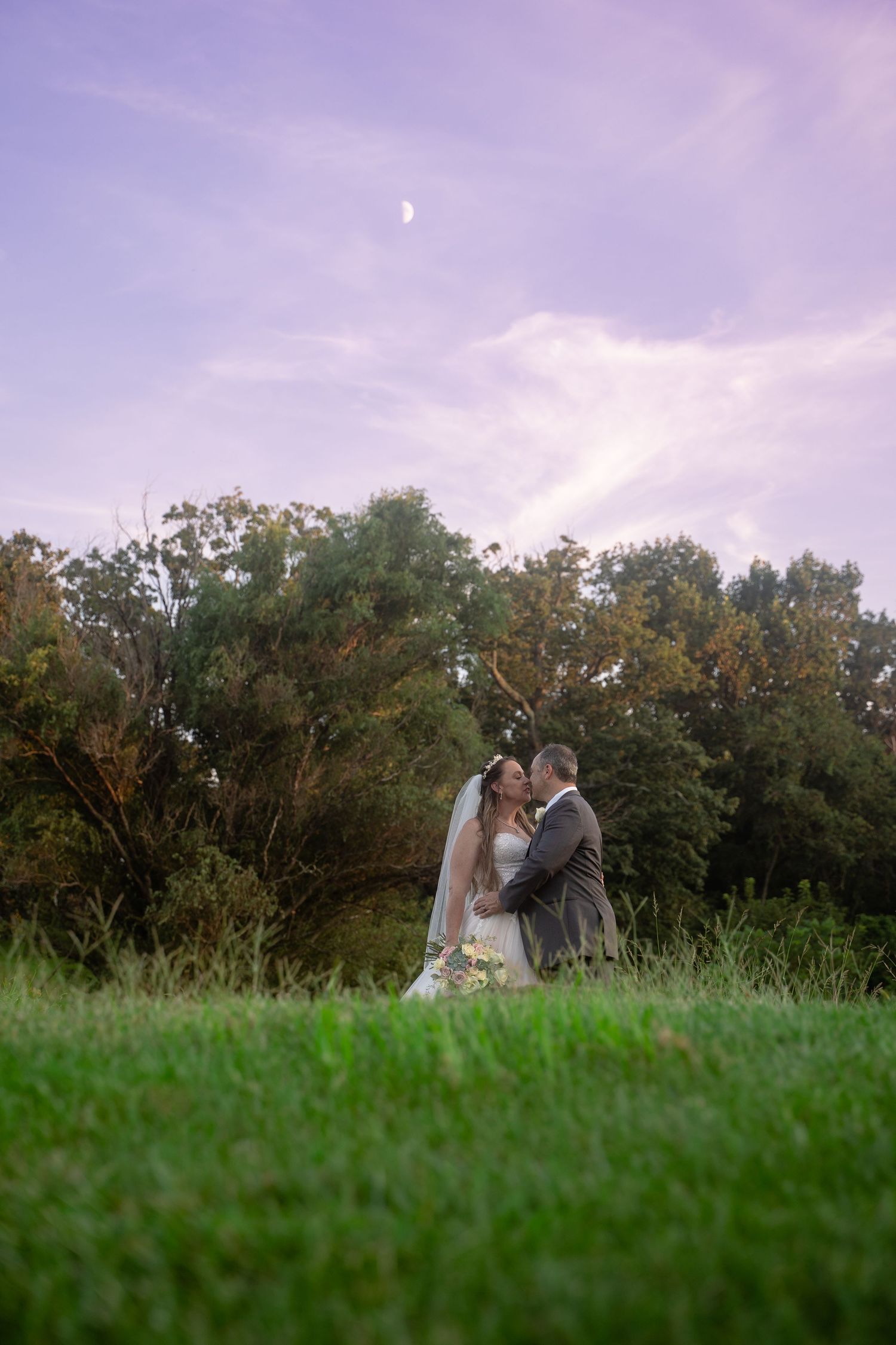 Emotional landscape of bride and groom kissing under a purple sunset during their elegantwedding in Northern Virginia