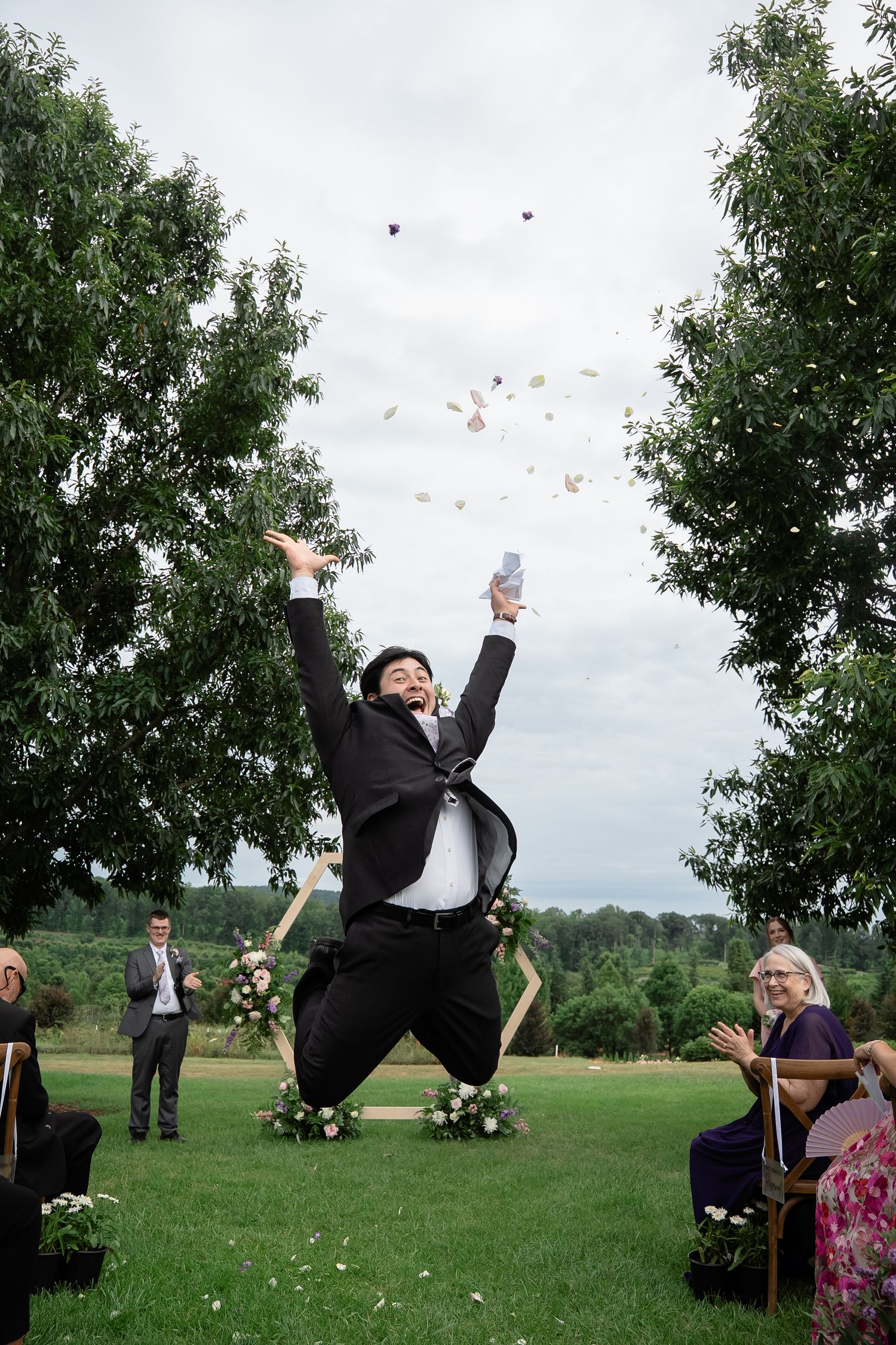 A groomsmen jumps in the air and throws flower petals in the air while recessing out of a wedding ceremony at The Market at Grelen