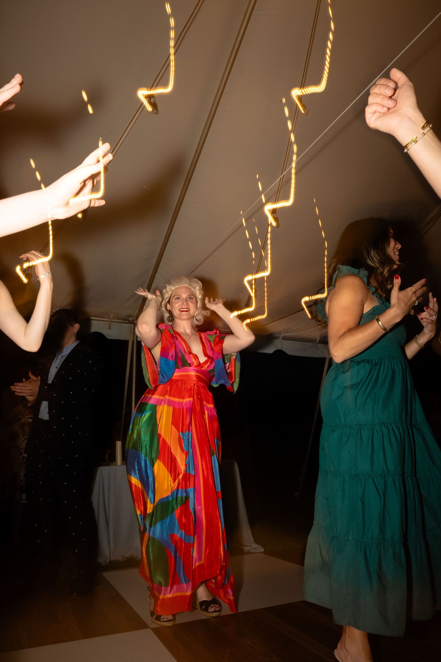 Wedding guest in colorful dress and colonial wig dances while long exposure light trails draw attention to her
