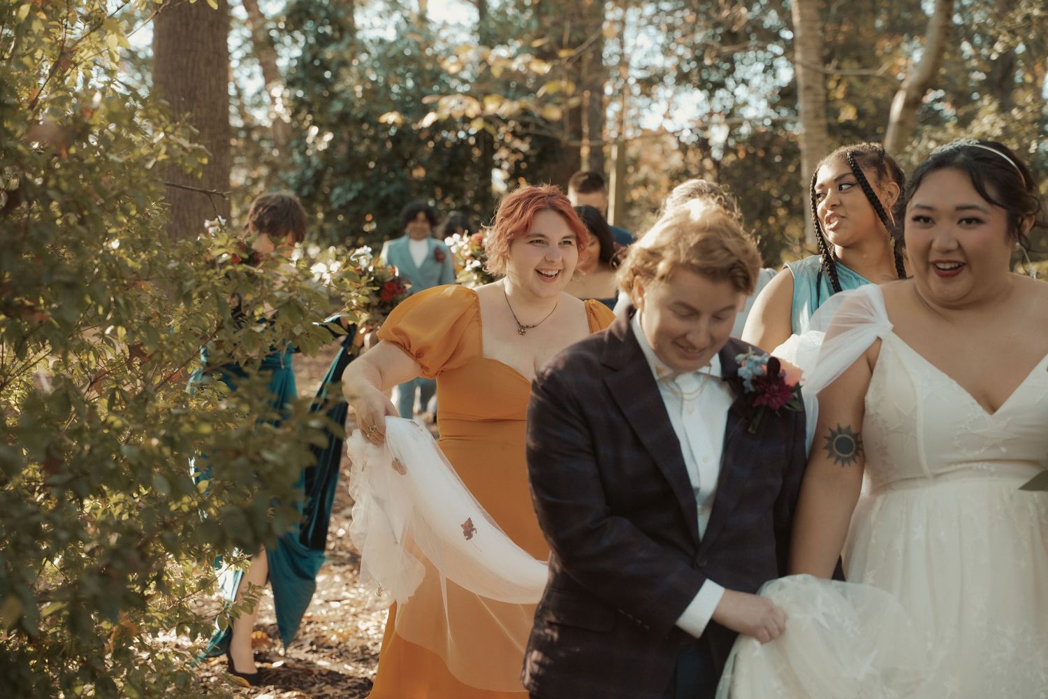 A bridesmaid smiles as she carries the bride's train on their walk to the ceremony space of the LGBTQ wedding in Maryland