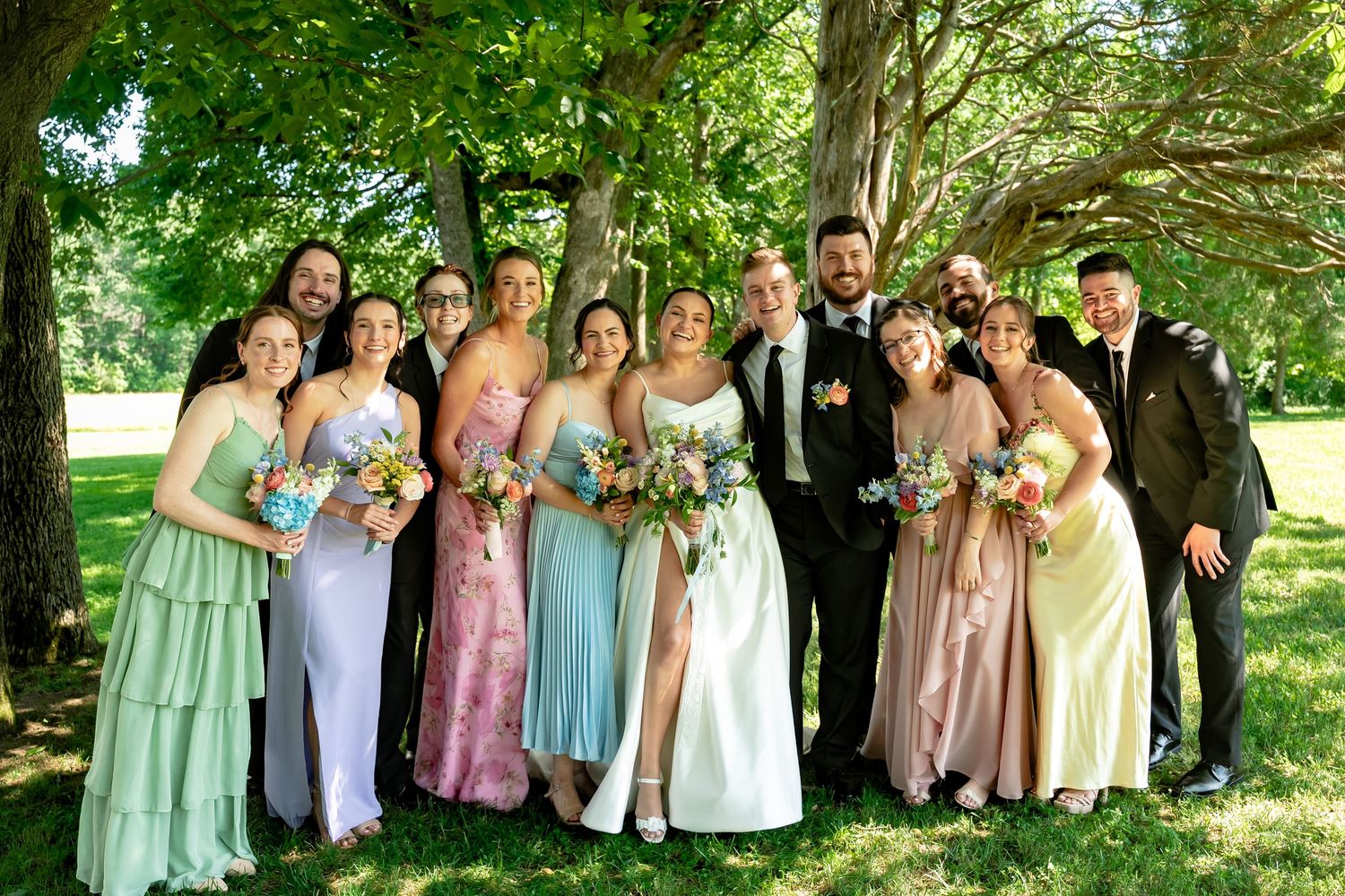 Bride and Groom are surrounded by bridesmaids in colorful dresses and groomsmen in dark suits for a group photo at Avonlea Farms