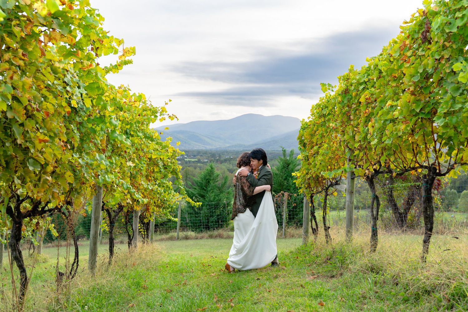 Queer couple hug in vineyard wedding photo session in Shenandoah valley with Blue Ridge mountains in background
