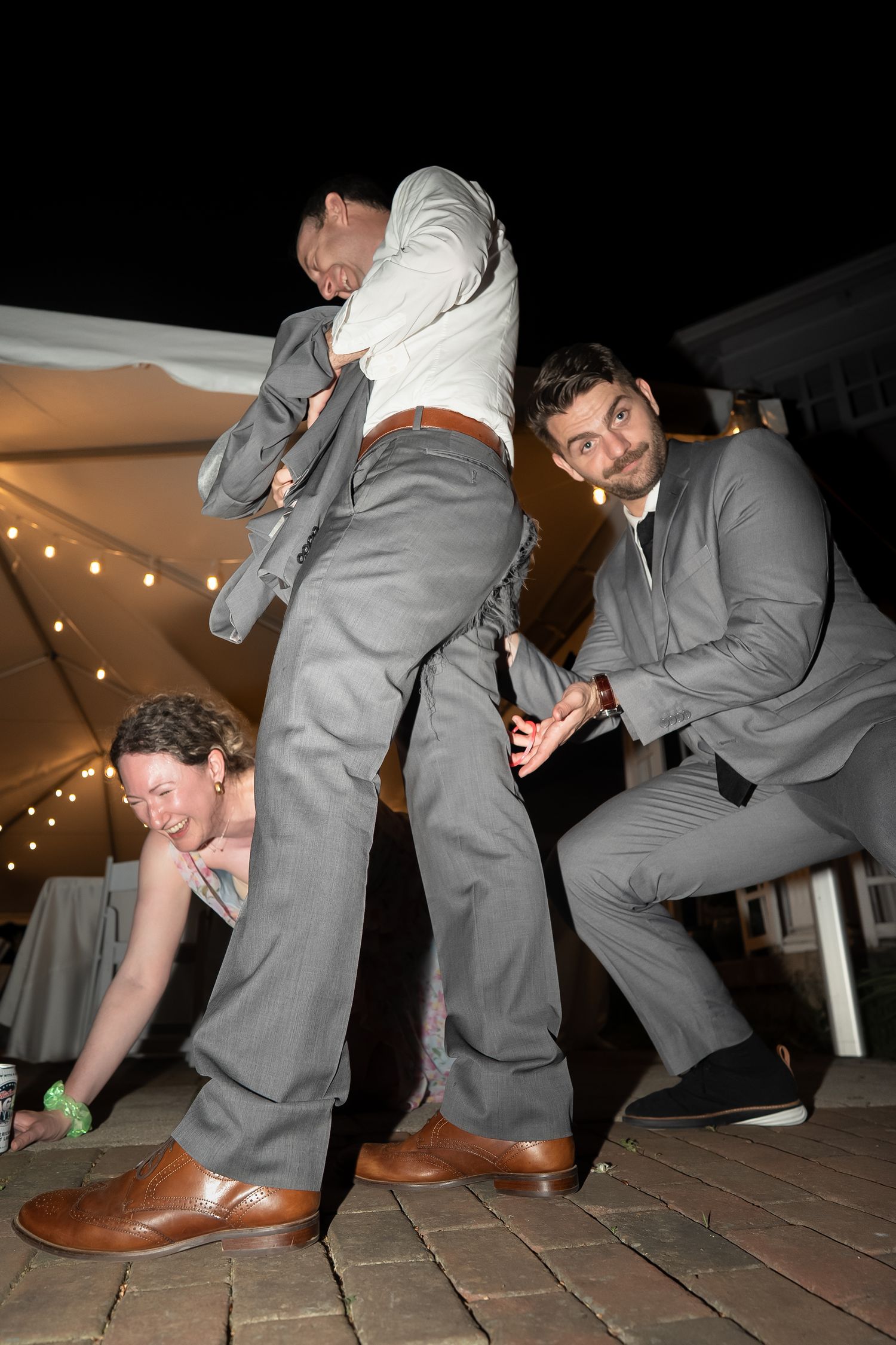 Goofy documentary style wedding photo of wedding guests laughing at bride's brother's ripped pants from having too much dancefloor fun